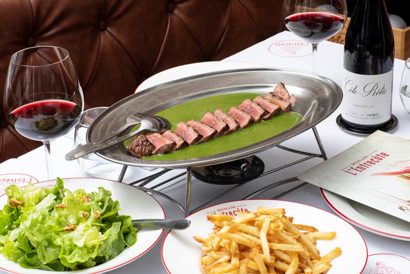 A steak, glass of red wine, bowl of lettuce and bowl of chips at Bouillon L'entrecote 
