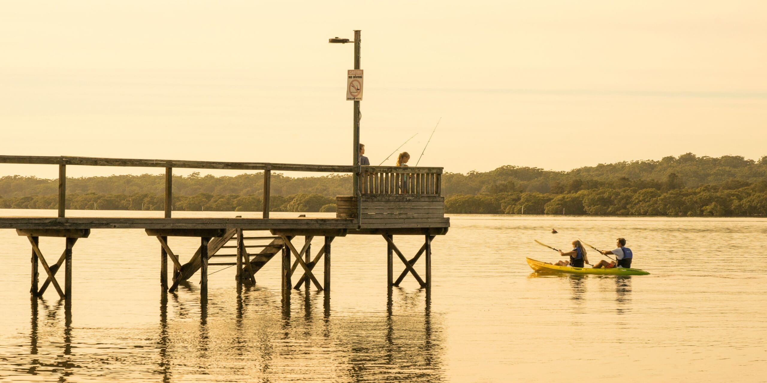 Couple kayaking along Tilligerry Creek by BIG4 Koala Shores Port Stephens Holiday Park at sunset. (Image Credit: Destination NSW).