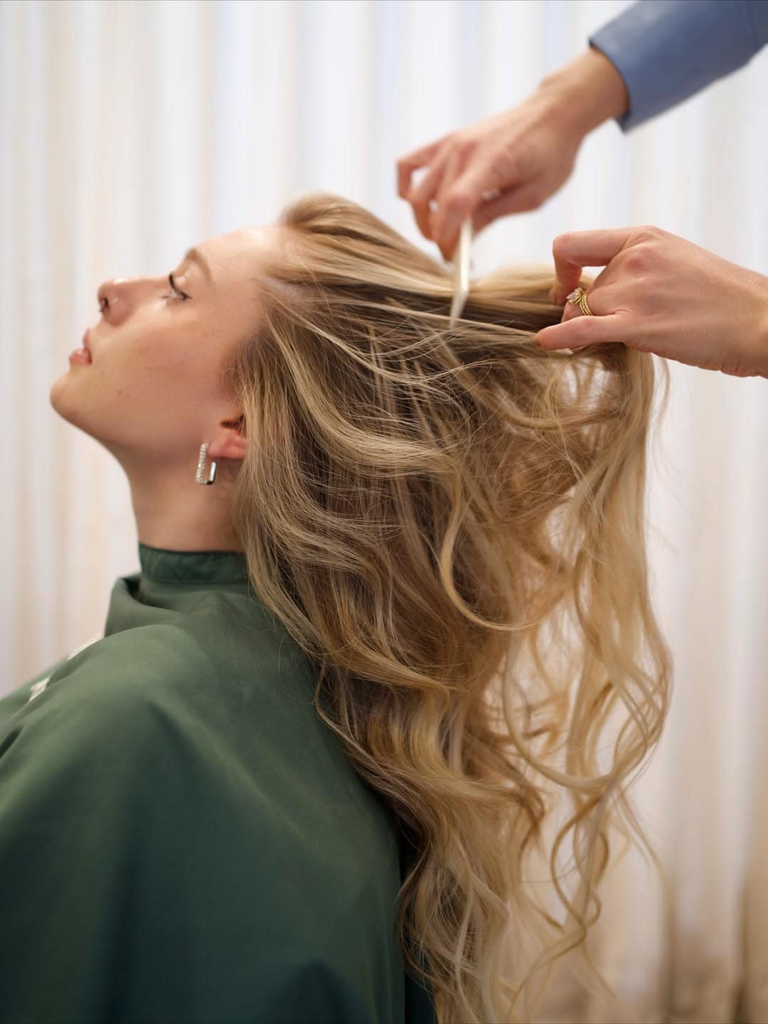 Polly and Stone stylist styling long blonde wavy hair with extensions on client in green salon cape Sydney