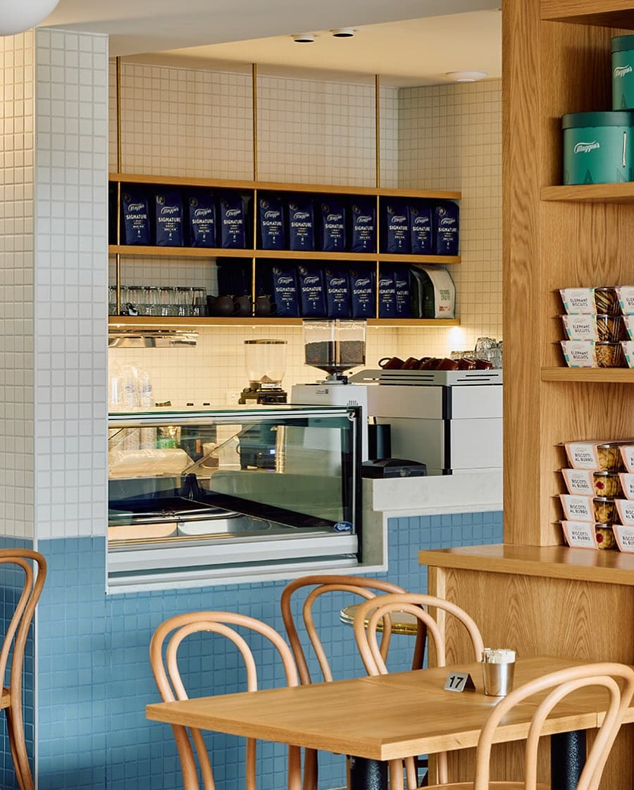 A blue wall, a coffee machine and tables at chairs inside the cafe.