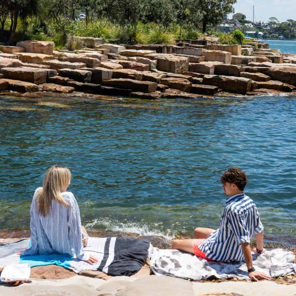 Two people sitting on the sandstone blocks next to marrinawi cove in barangaroo