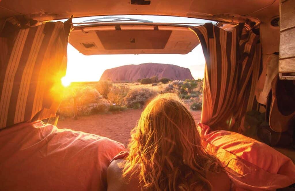 Someone with long hair peering out the back of their van to Uluru.