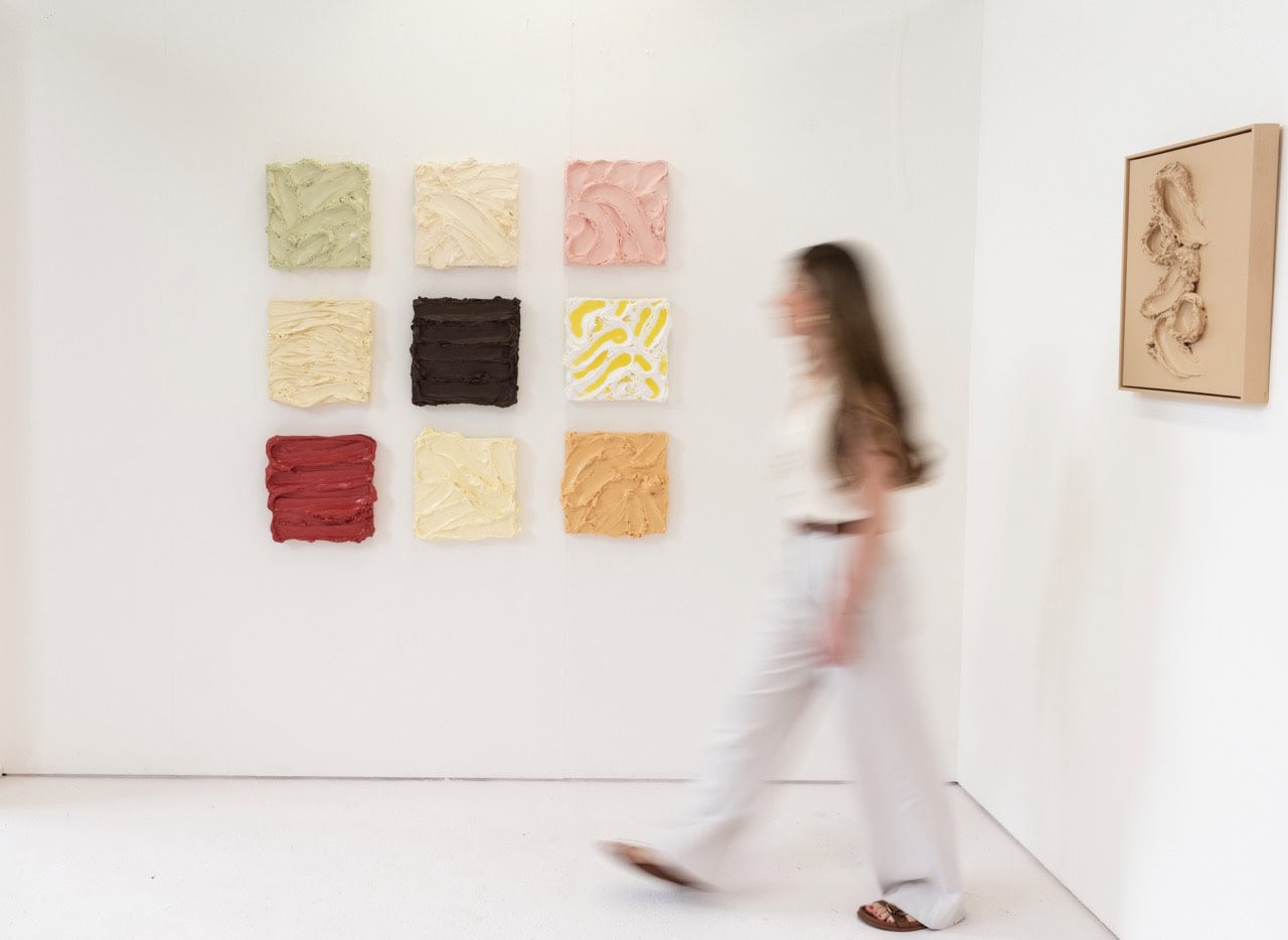 Artist Marie Aubeline Hiot walking past nine of her textured artworks