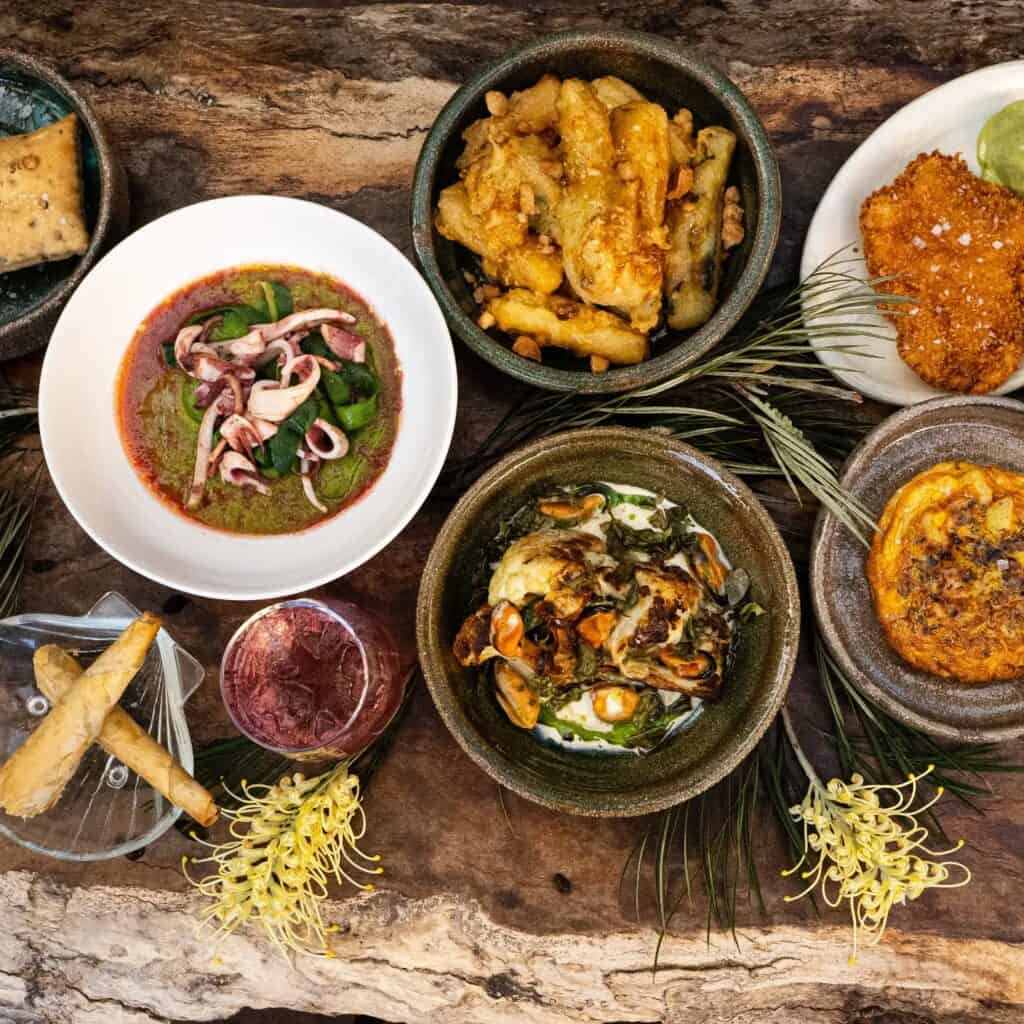 A feast of dishes on a wooden table, decorated with native flowers, at Bush in Redfern. 
