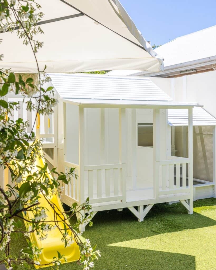 A white-washed cubby house and yellow slippery dip.