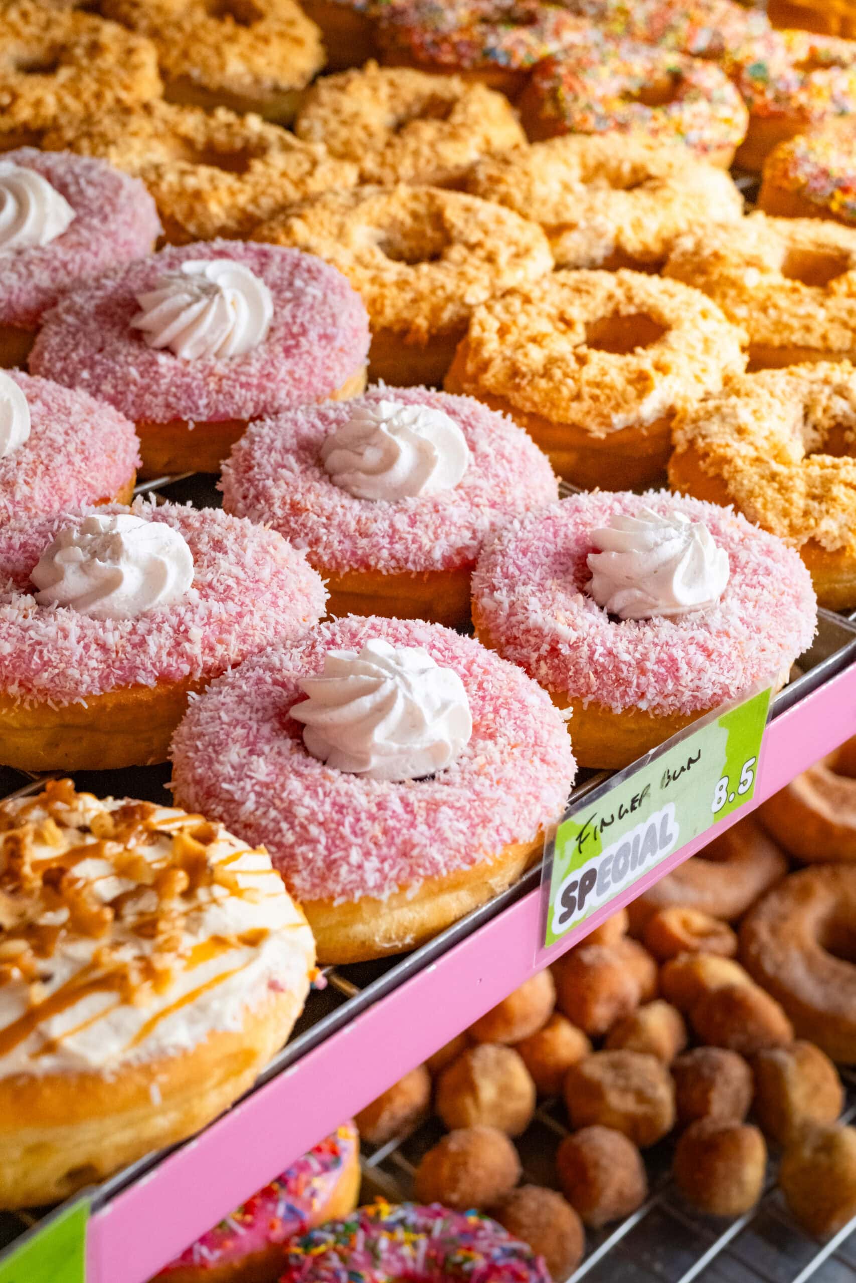Display cabinet of pink coconut finger bun donuts crumble ring donuts and cinnamon donut holes at Grumpy Donuts St Peters Sydney