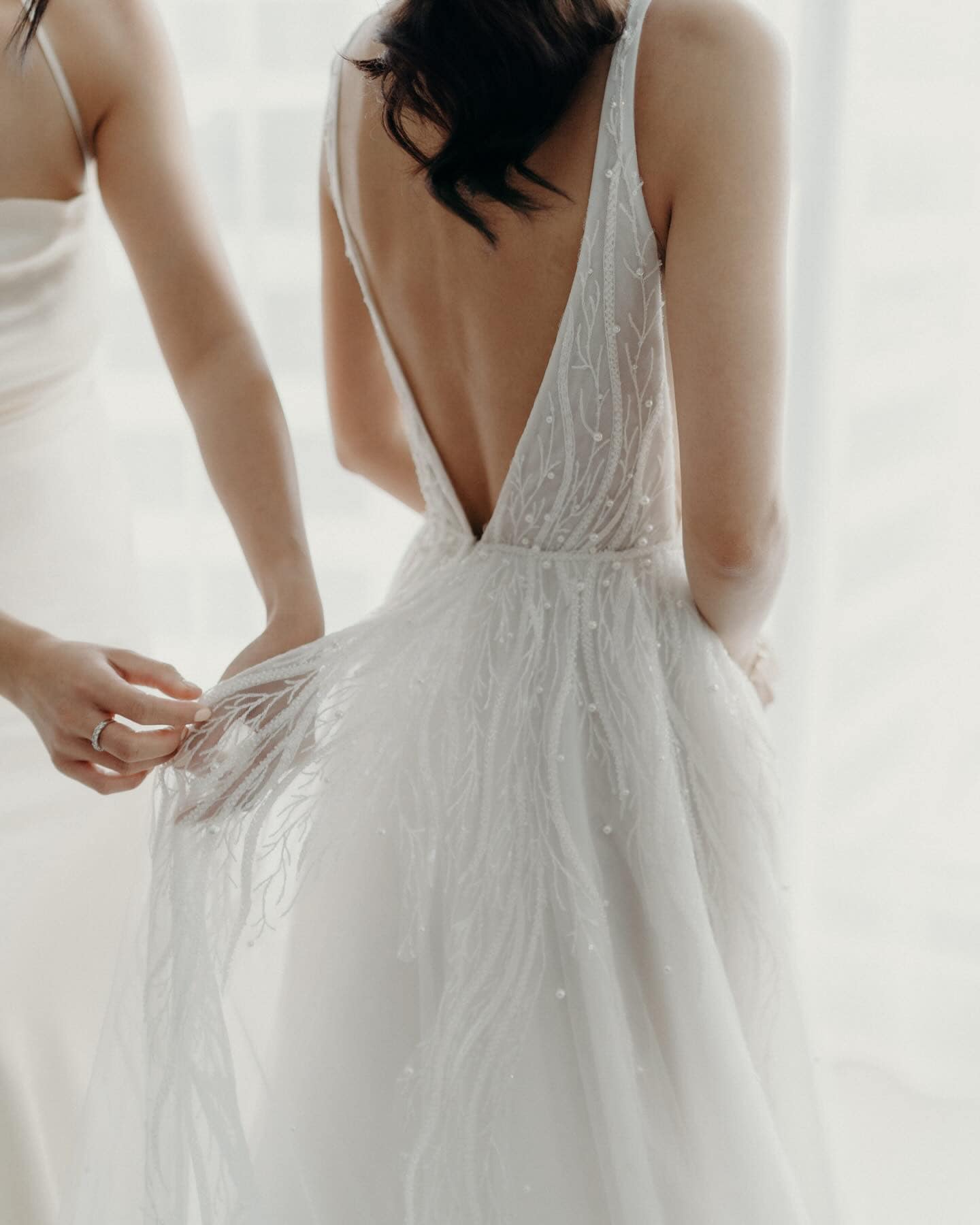 A fitting of a wedding dress with a deep V back, with someone making adjustments.