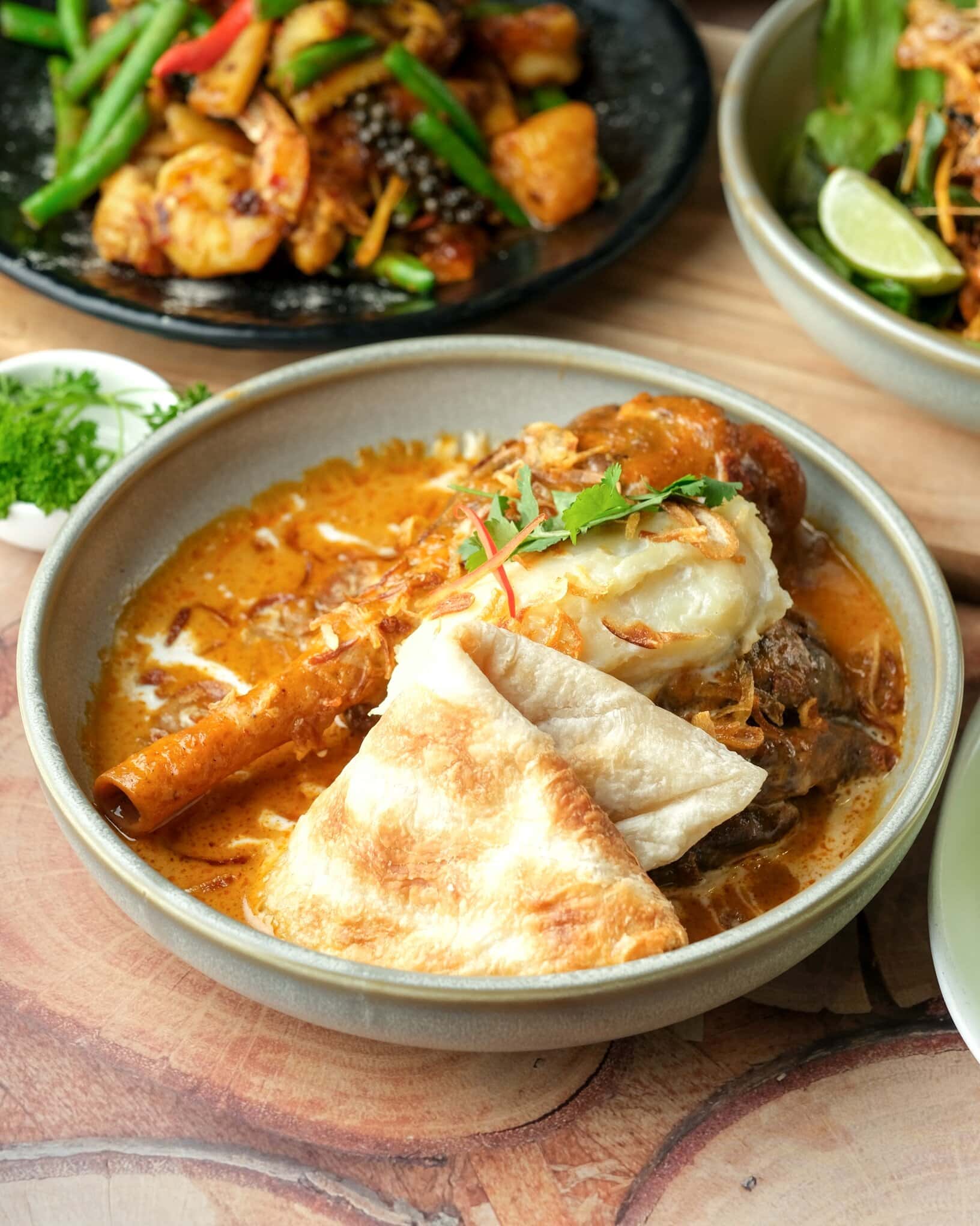 A massaman lamb shanks dish with roti on a brown table.