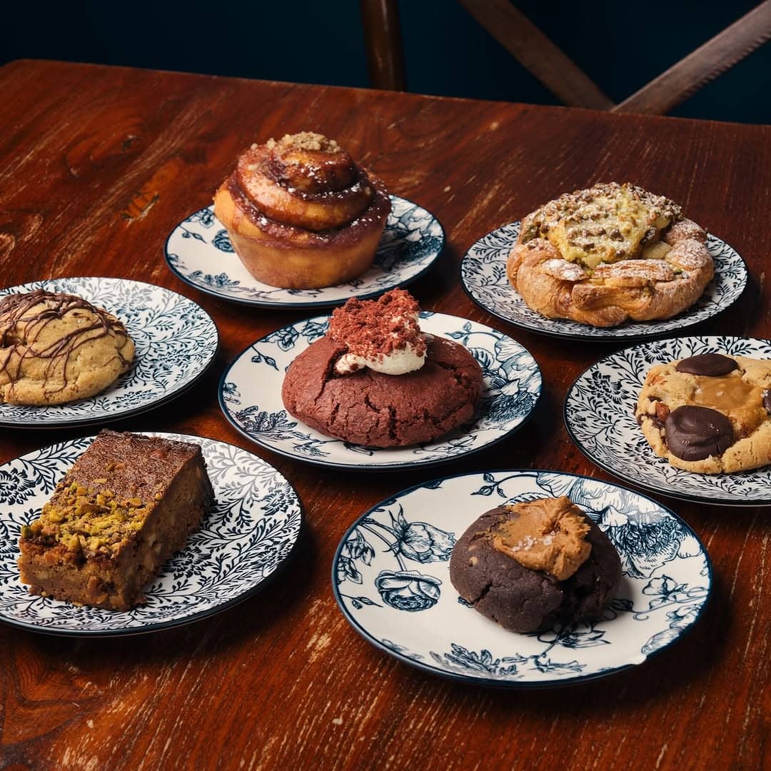 A brown table with seven blue and white plates, all bearing sweet baked treats.