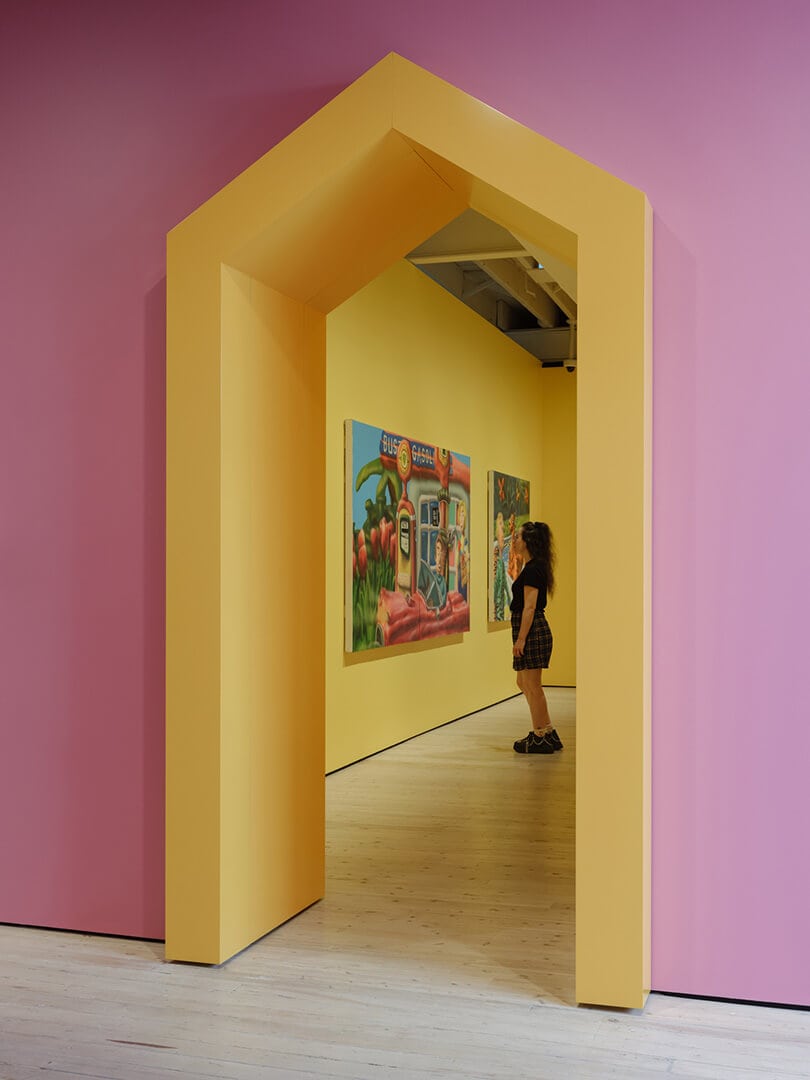 A person looks at a bright artwork on a yellow wall.