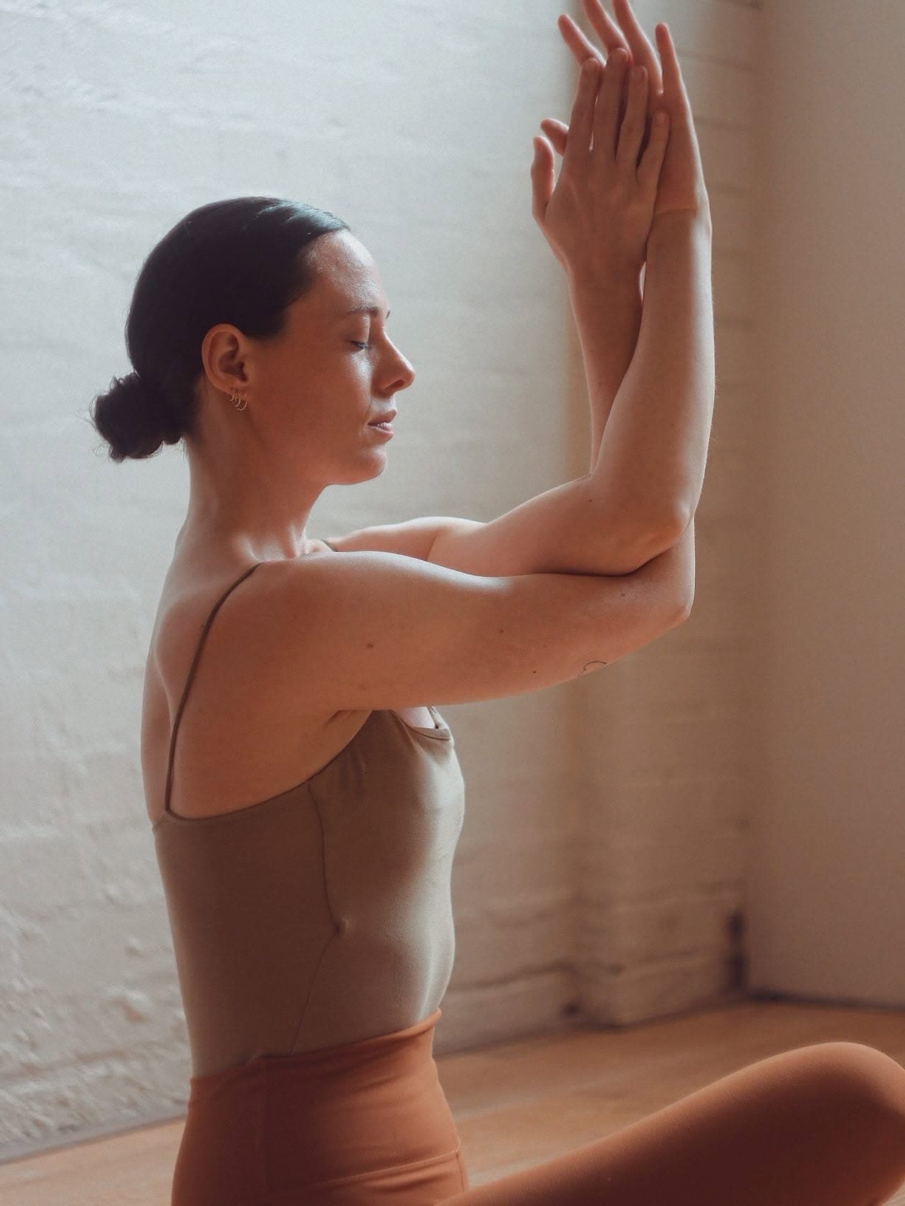 Woman practising an eagle-arm yoga pose against a textured studio wall