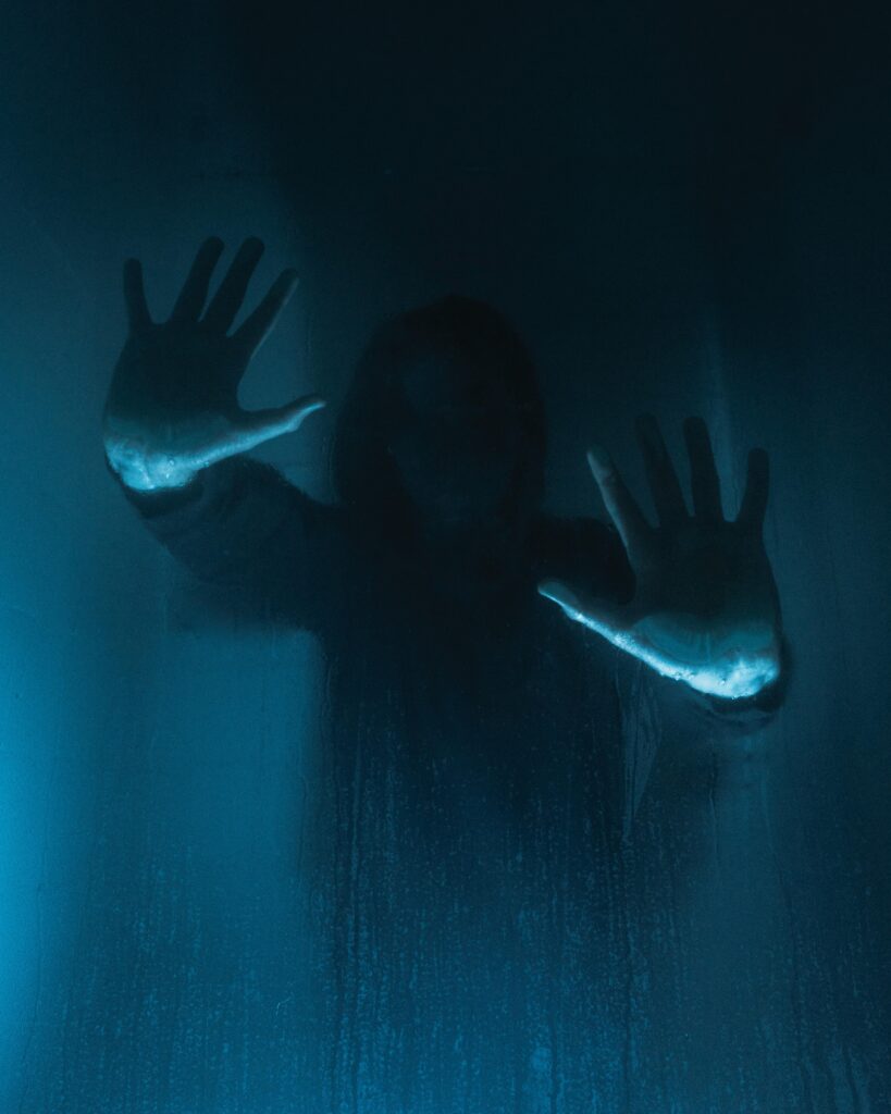 An eerie woman has her hands up against the glass in a horror scene