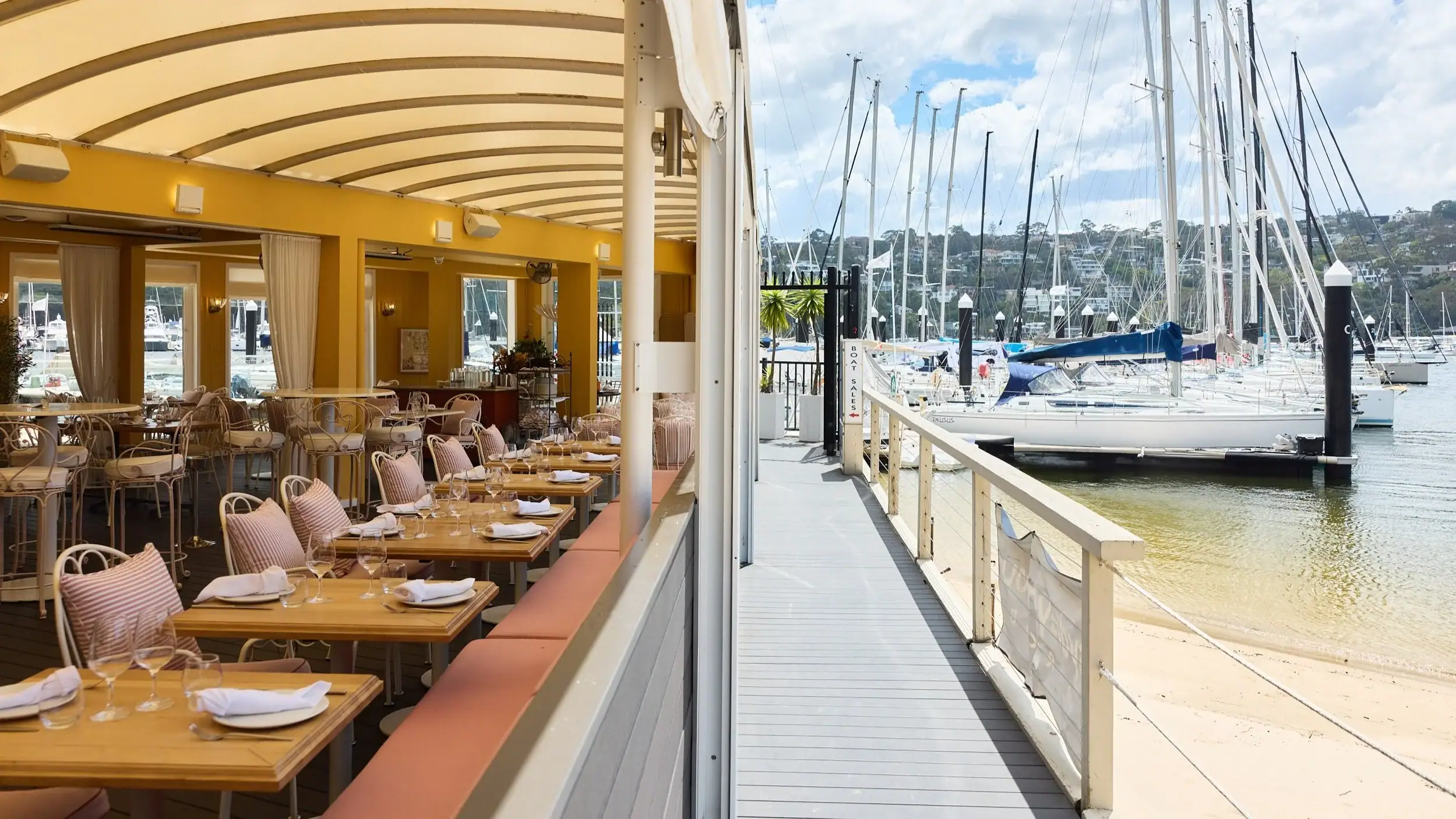 Waterfront dining room with striped awning pink cushioned banquettes and marina sailboat views at St Siandra The Spit Mosman Sydney