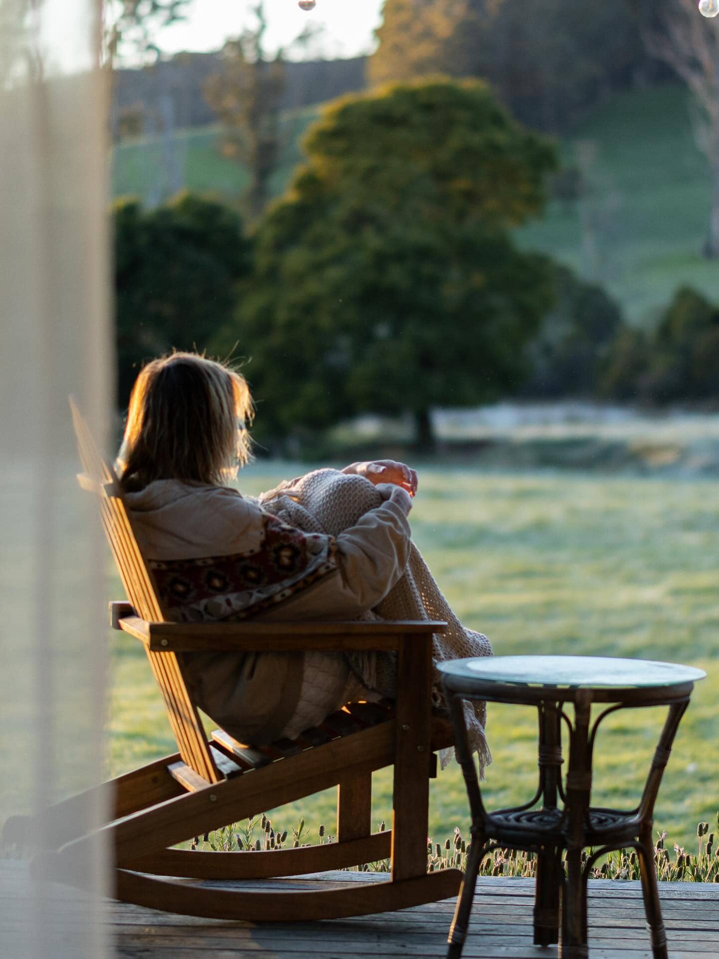 woman curled up on chair outside the sawmiller's cottage in tasmania near bridport