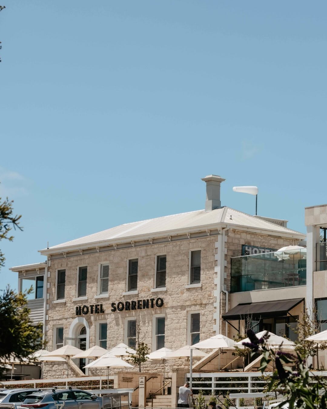 Historic limestone façade of Hotel Sorrento, with outdoor dining terraces and white umbrellas overlooking the seaside village.