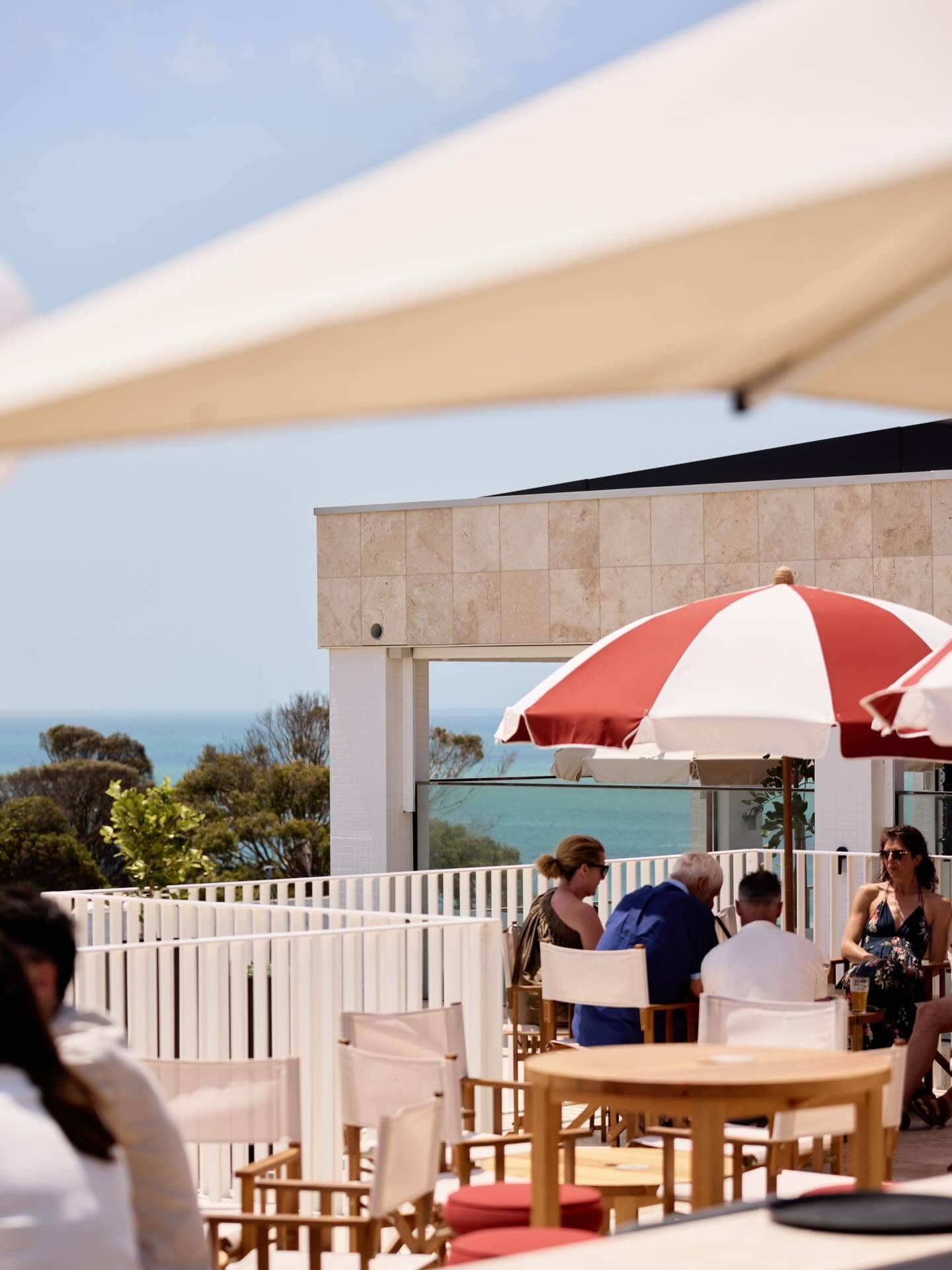 Sun-drenched rooftop terrace at Hotel Sorrento featuring striped umbrellas, outdoor dining and views towards Port Phillip Bay.