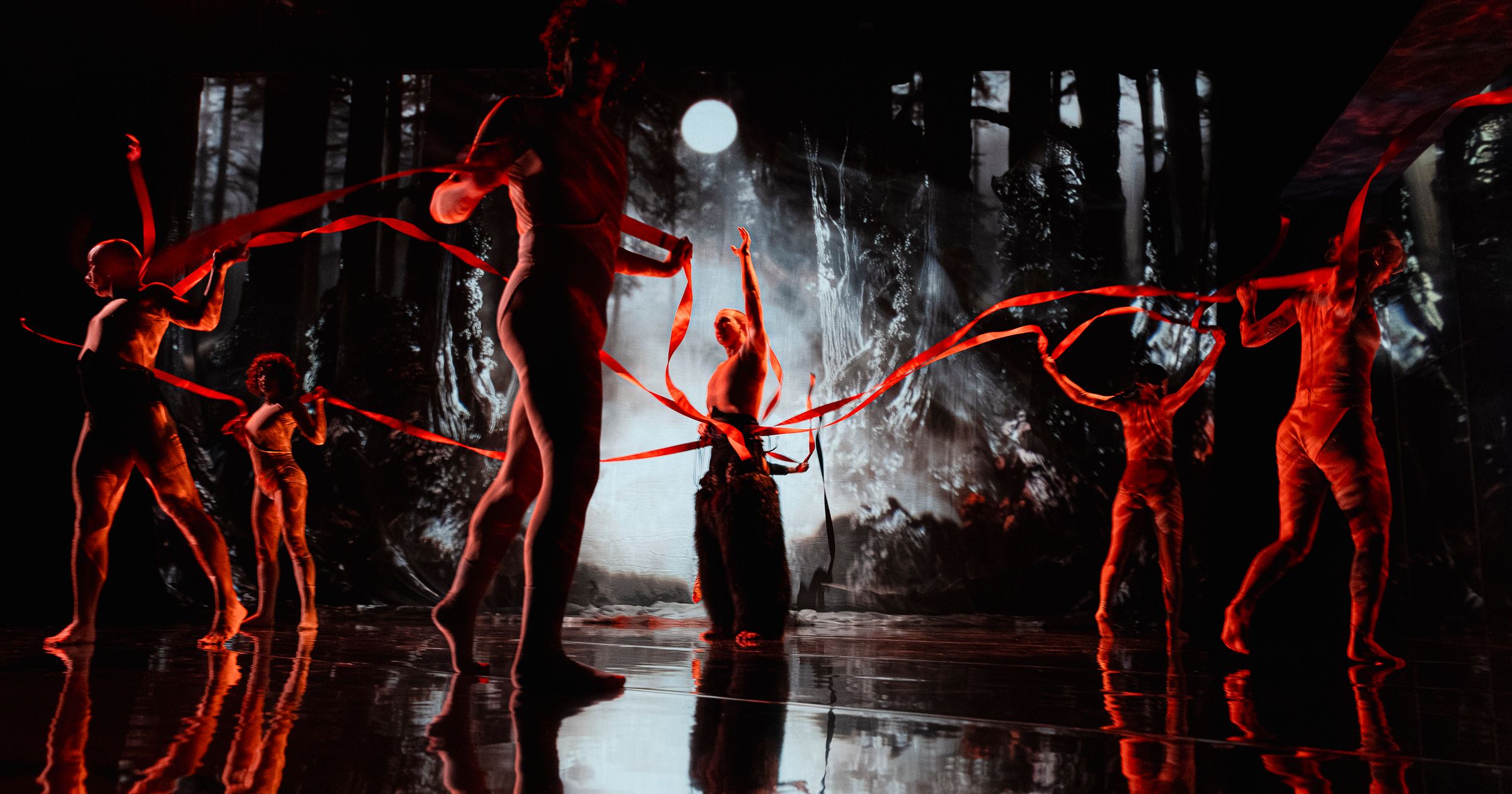 Silhouetted dancers moving with red ribbons beneath a glowing moon for The Forest at RISING Melbourne.