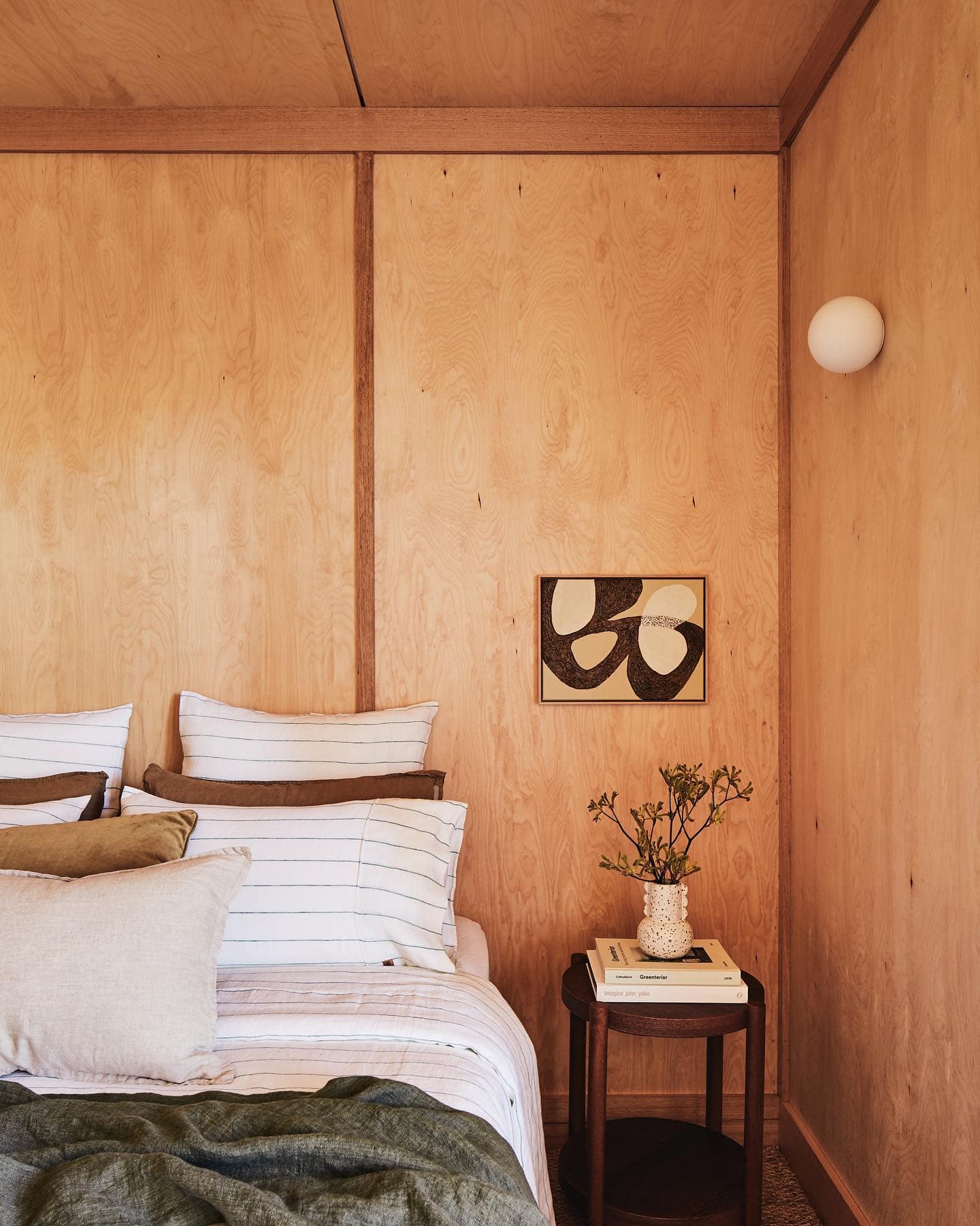 Cosy bedroom at YOKO Luxury Cabin on the Mornington Peninsula, featuring natural plywood walls, striped linen bedding and minimalist artwork.
