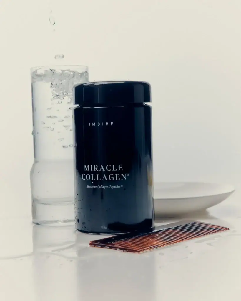 A midnight blue can of miracle collagen powder from imbibe next to a bubbling glass of water