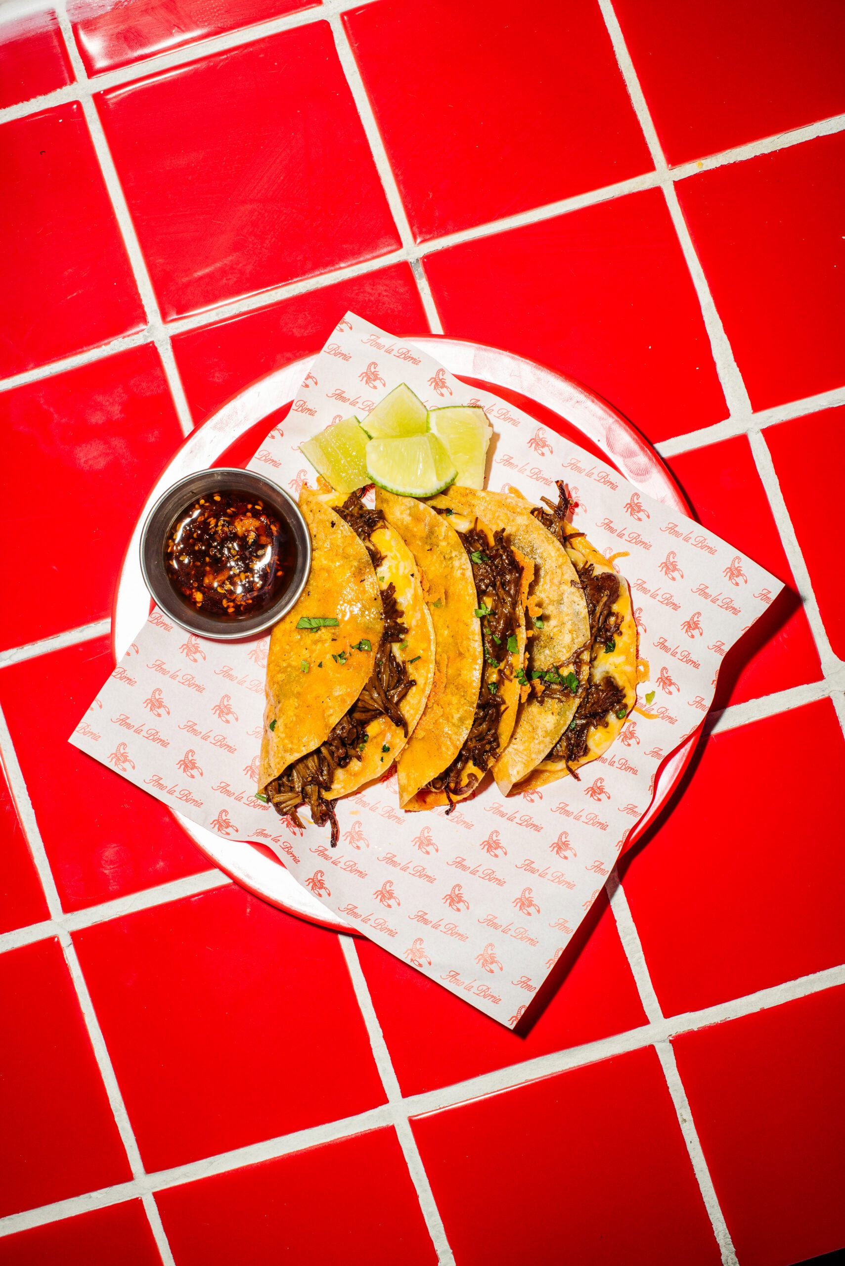 birria tacos with side salsa on a red table