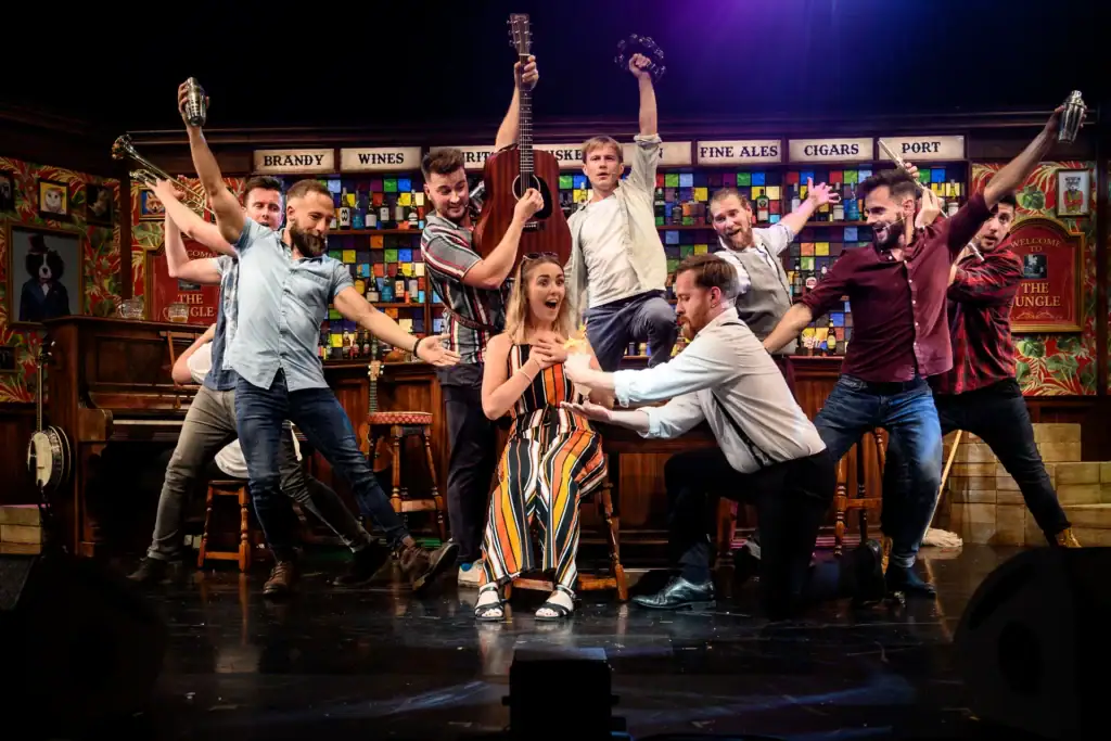 Eight male performers serenading a woman sitting on a chair as part of The Choir of Man performance.