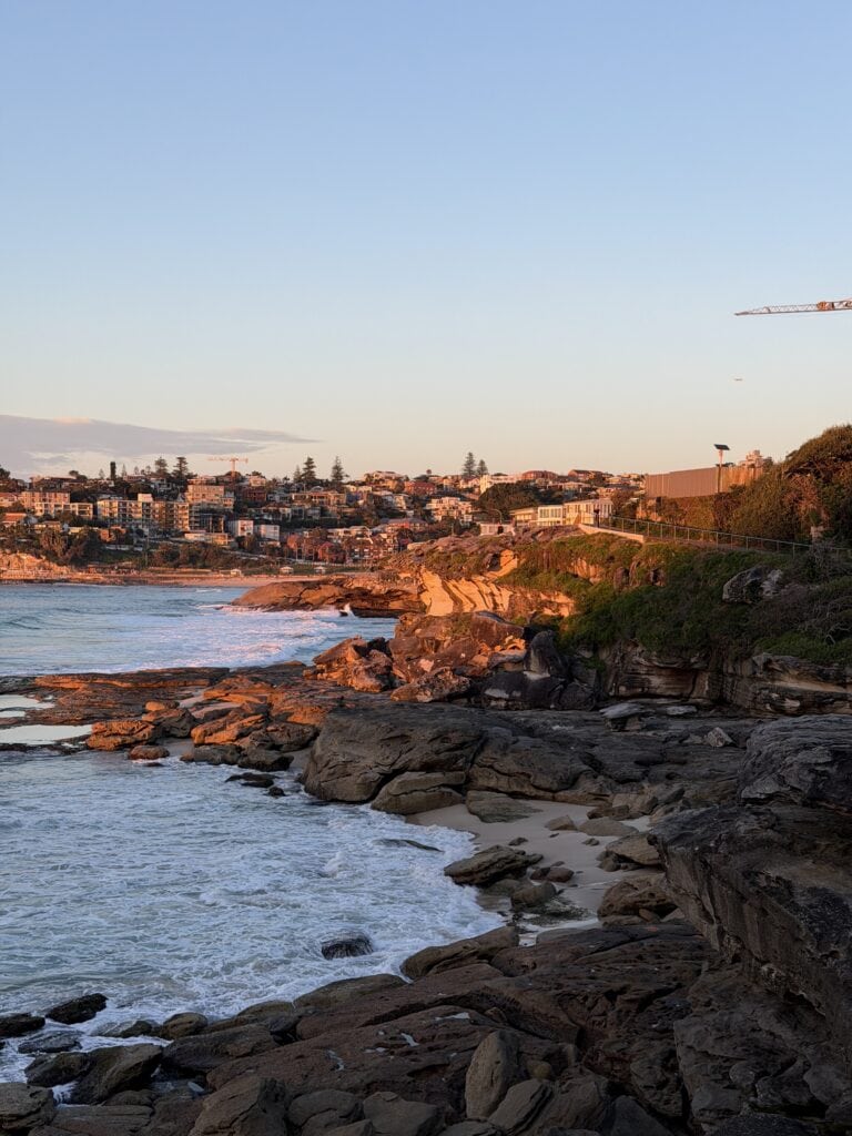 Sandy Mackenzie's Bay beach appearing between the rocks at sunset with coastal suburbs in the background, Tamarama, Sydney