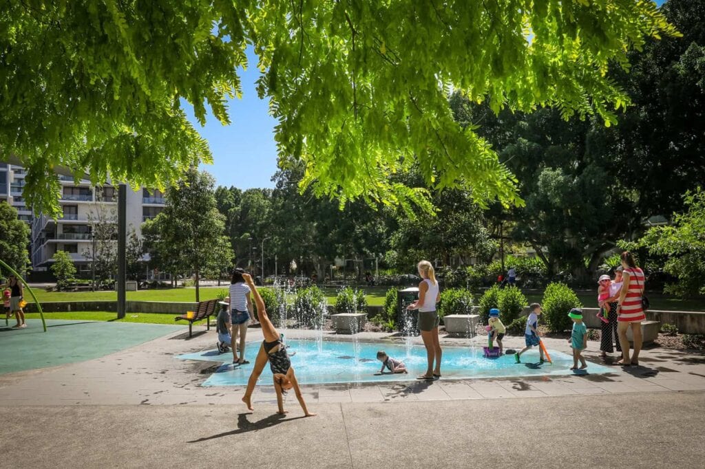 Children playing in the waterplay section of May O'Brien Reserve in Zetaland as adults watch on.