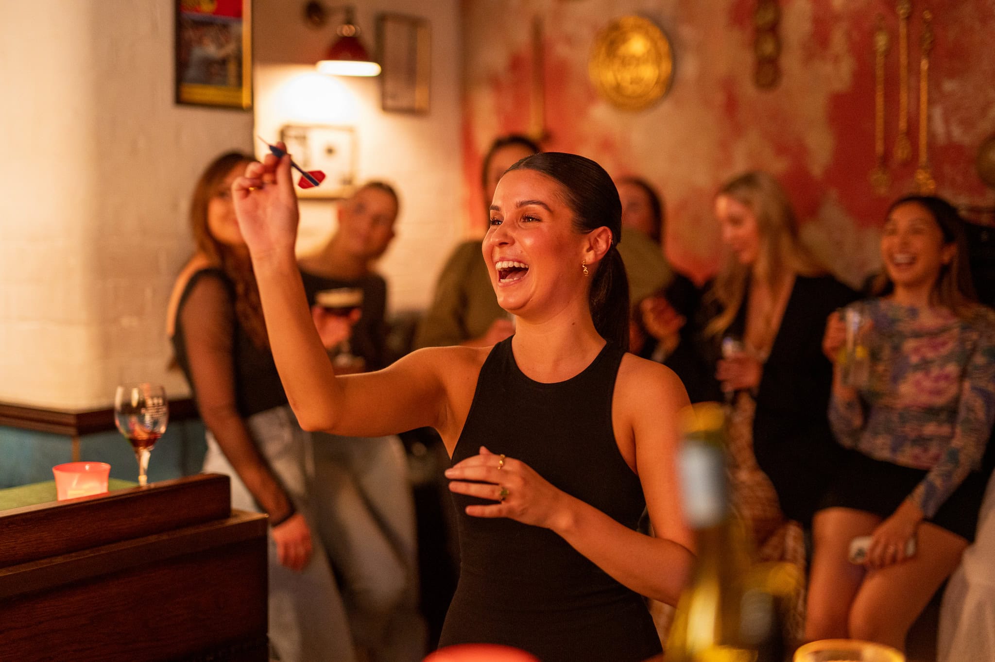 Woman laughing while throwing dart with crowd of friends at Flight Club The Rocks Sydney