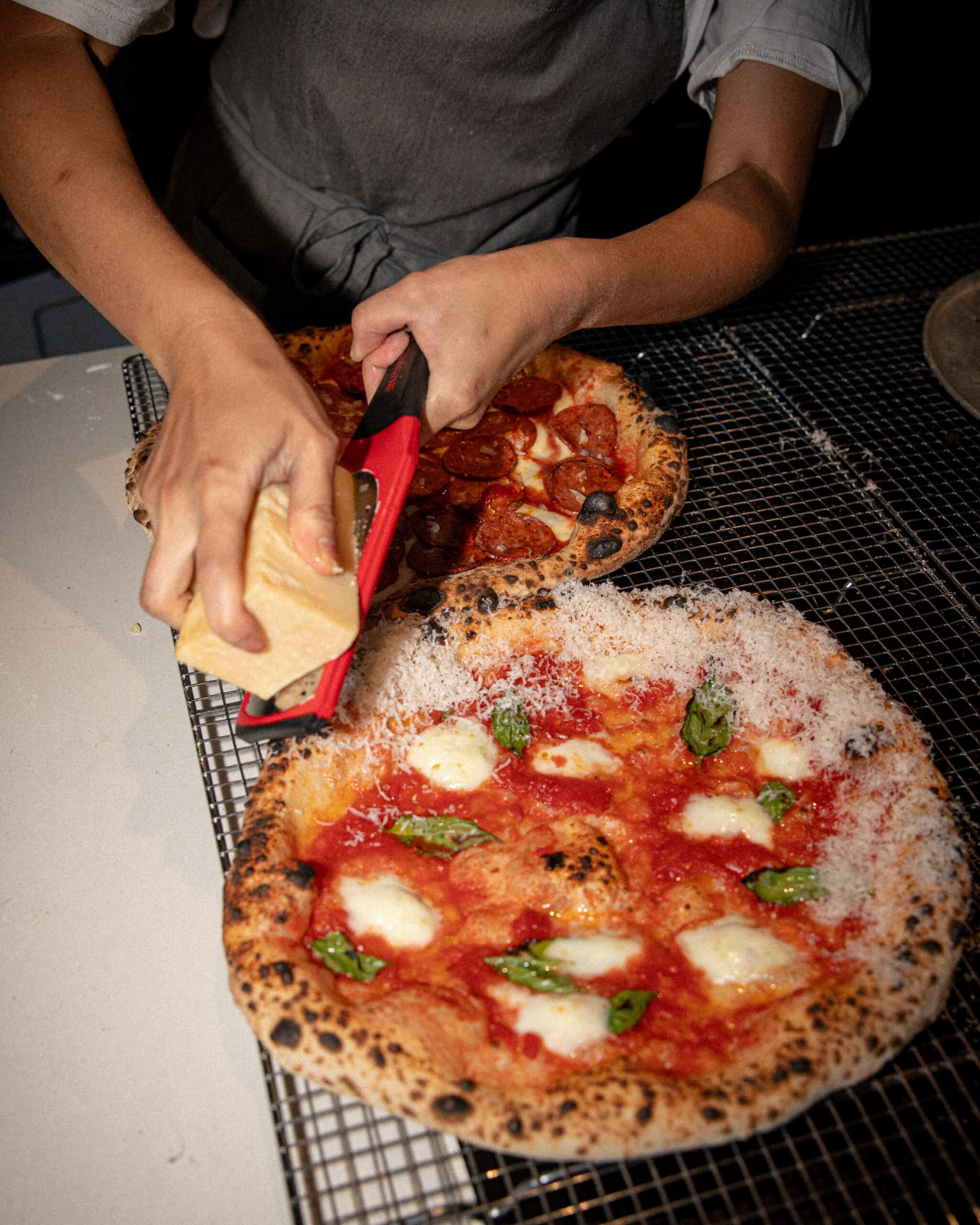 Chef grating parmesan over a sourdough margherita pizza beside a pepperoni pizza at Pizzeria Officina, Braddon Canberra