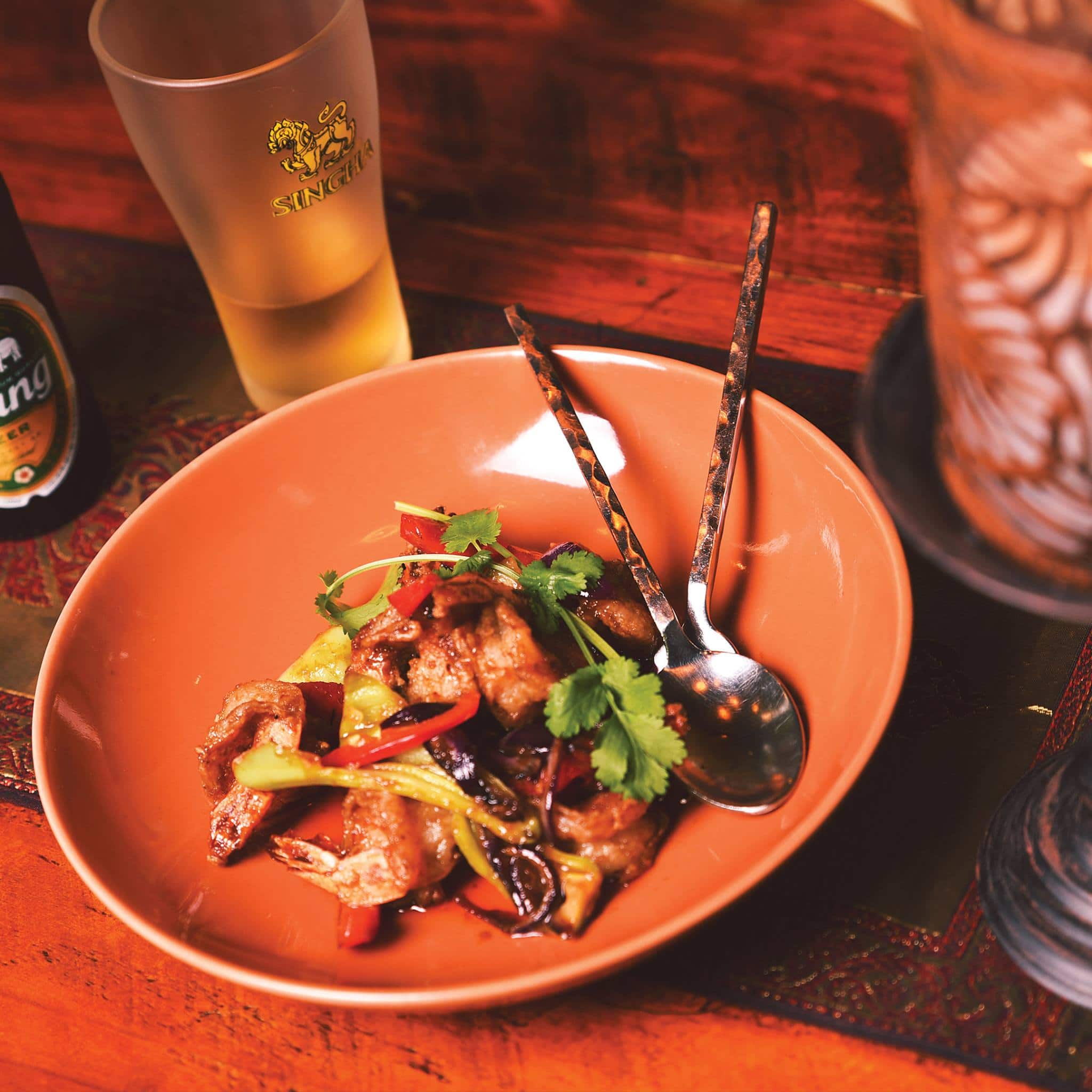 A Sabai Cafe stir-fry served in a terracotta bowl paired with a Singha beer at Sabai in Adelaide.