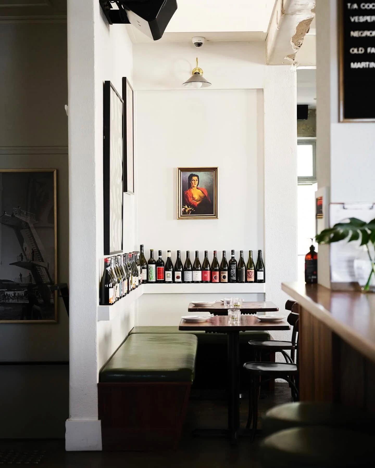 Bar Rochford dining room with green leather booth seating row of wine bottles on ledge and portrait painting Canberra