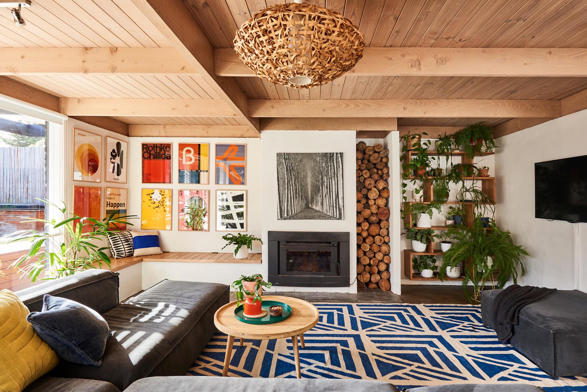 Living room at 100 Steps to the Beach in Anglesea, with exposed timber ceilings, fireplace, indoor plants and colourful modern art.