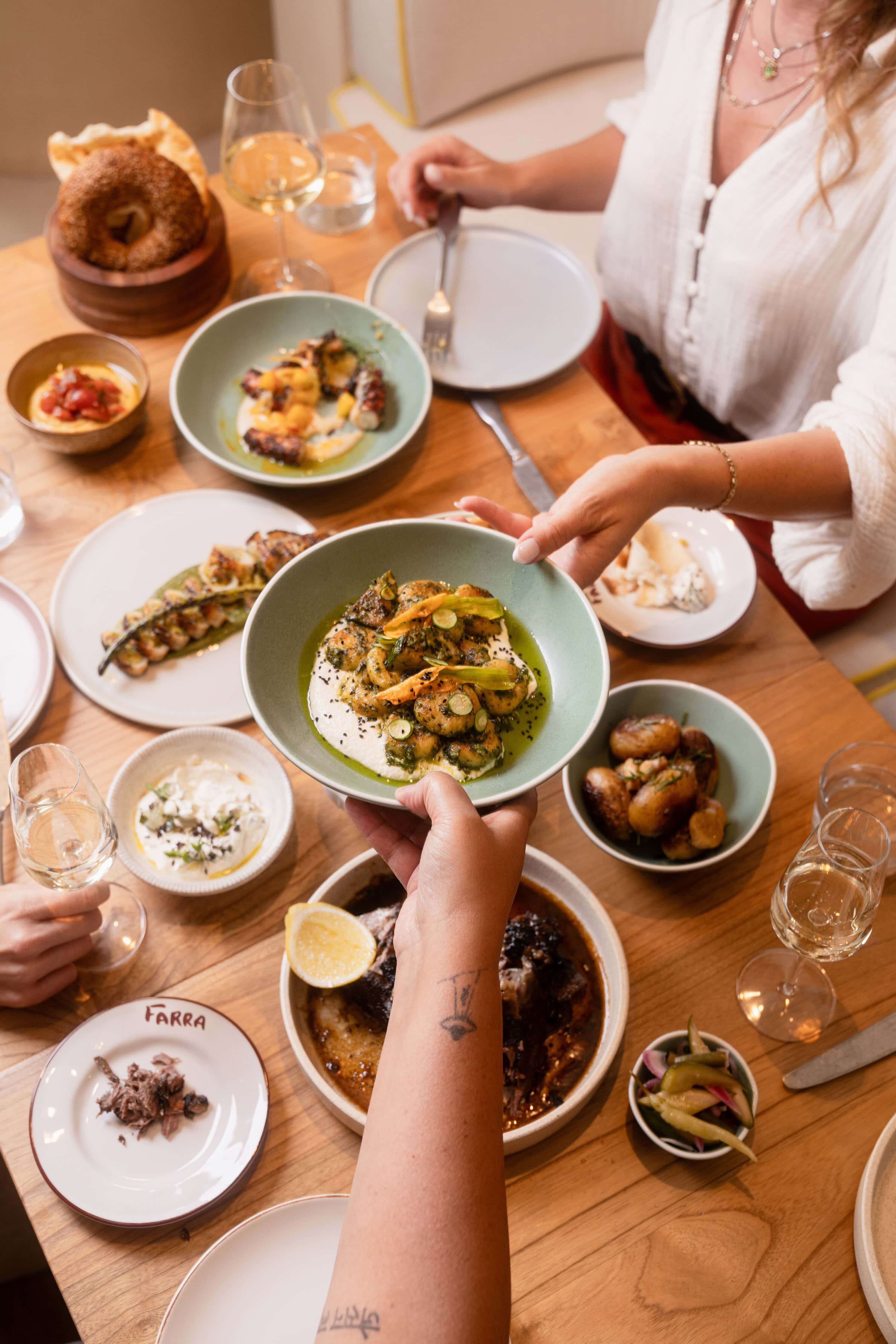 A diner hands a plate of mizithra dumplings over a table at FARRA restaurant in Perth