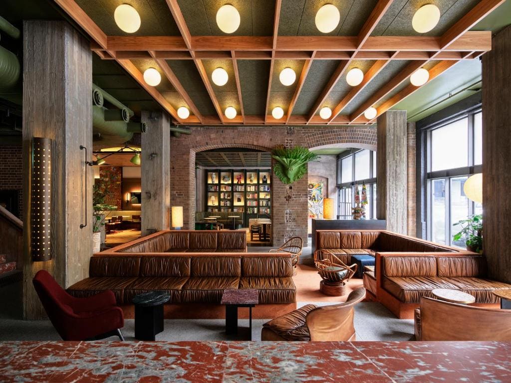 The industrial-style lobby at the ace hotel in sydney, featuring circular globe lights, a leather couch and exposed brick walls.
