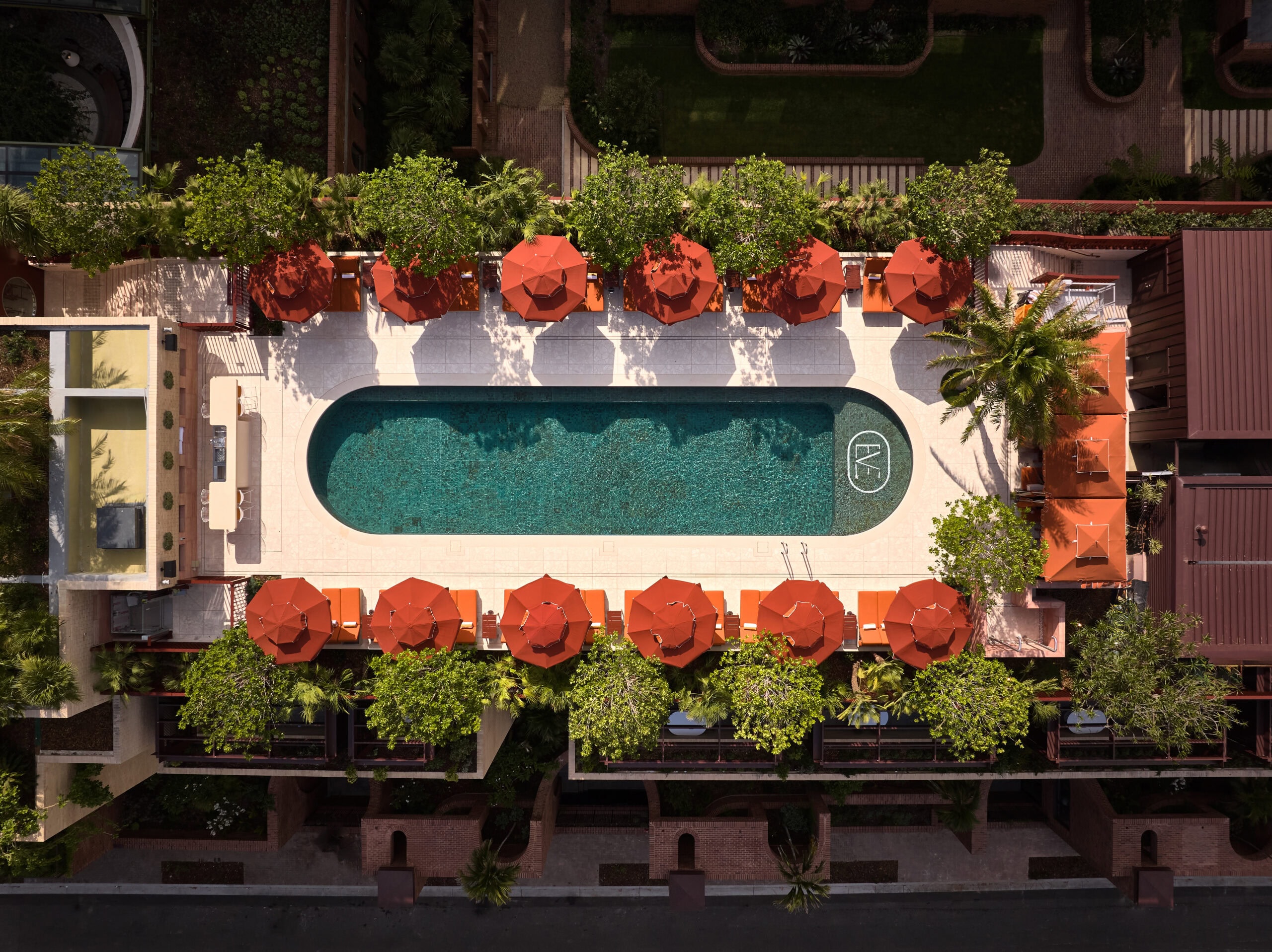 An aerial view of Eve Hotel's rooftop pool, surrounded by orange pool-side umbrellas and greenery.