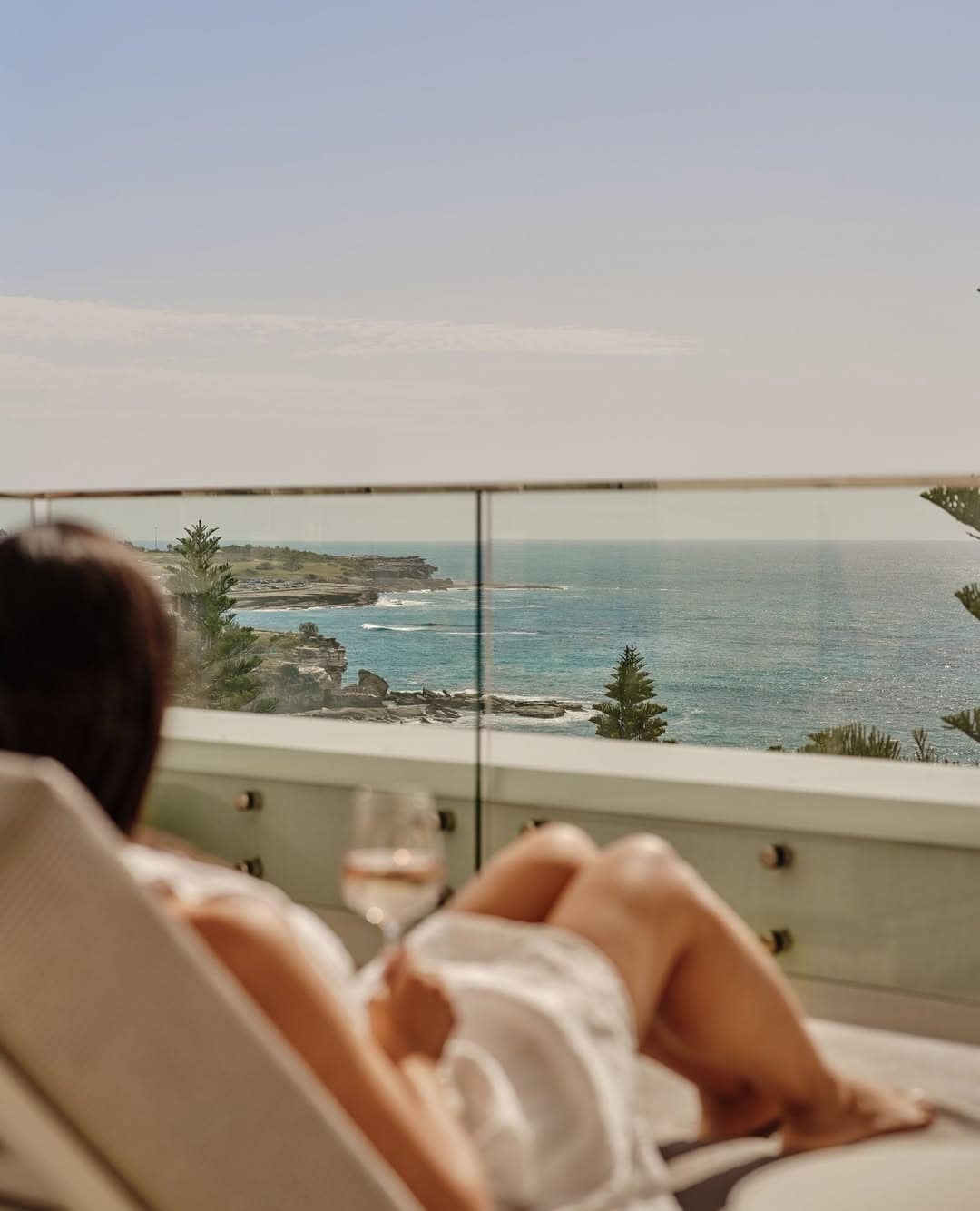A woman enjoying a glass of wine, enjoying ocean views from the balcony of Intercontinental Coogee.