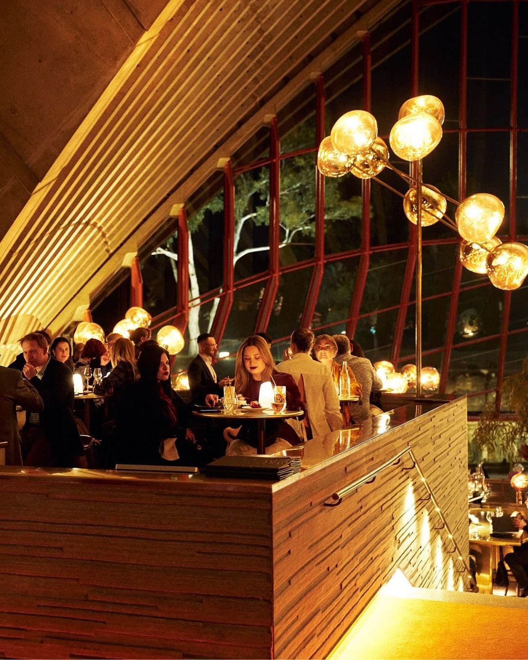 Diners soaking up the ambience at Bennelong in Sydney, featuring the unique dining room shaped by the opera house's sails.