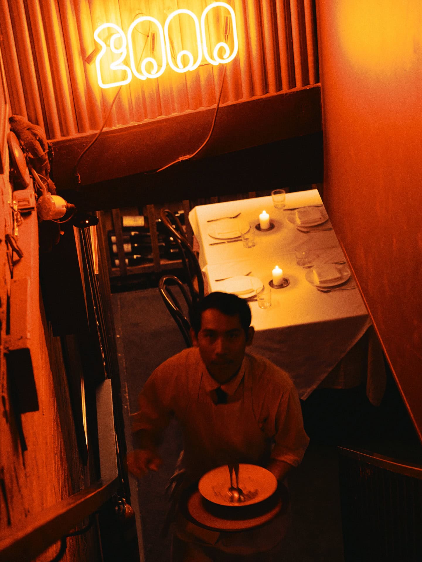 A top down view of a waiter clearing tables with the pellegrino 2000 neon sign in the background.
