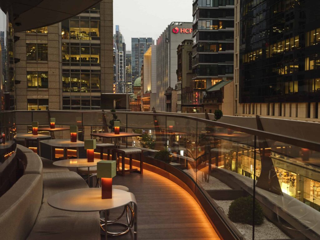 The outdoor seating area of Sydney rooftop bar Joji at dusk, overlooking the city lights.