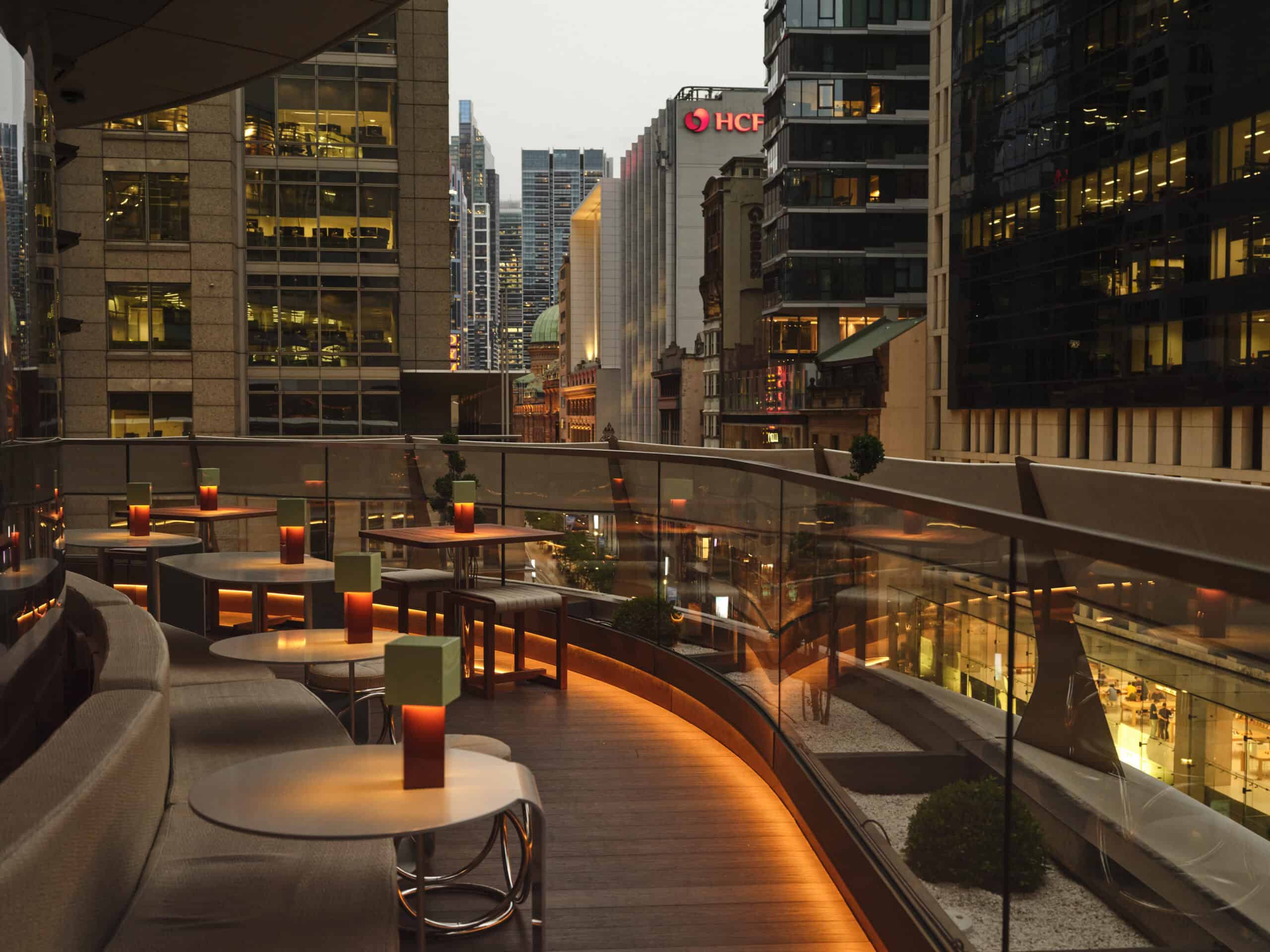 The outdoor seating area of Sydney rooftop bar Joji at dusk, overlooking the city lights.