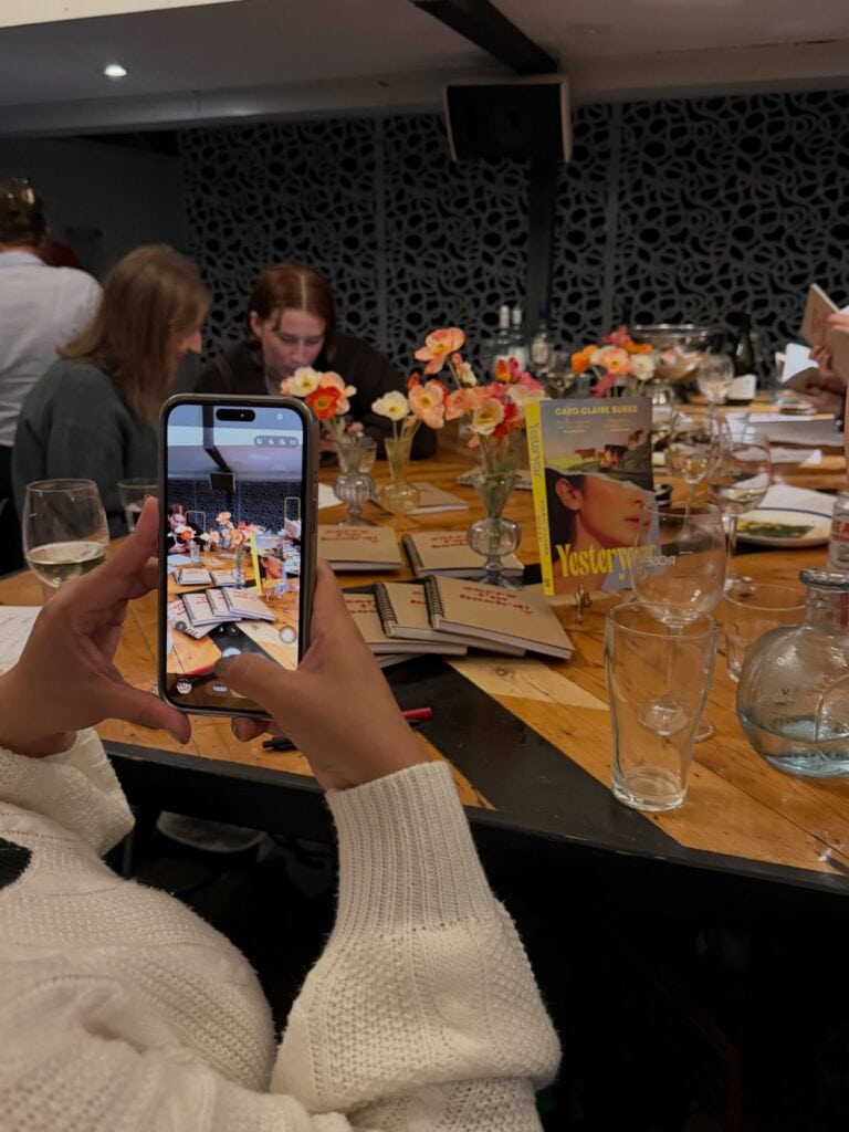 Sorry I'm Book'd book club members at dinner table with Yesteryear by Caro Claire Burke and notebooks