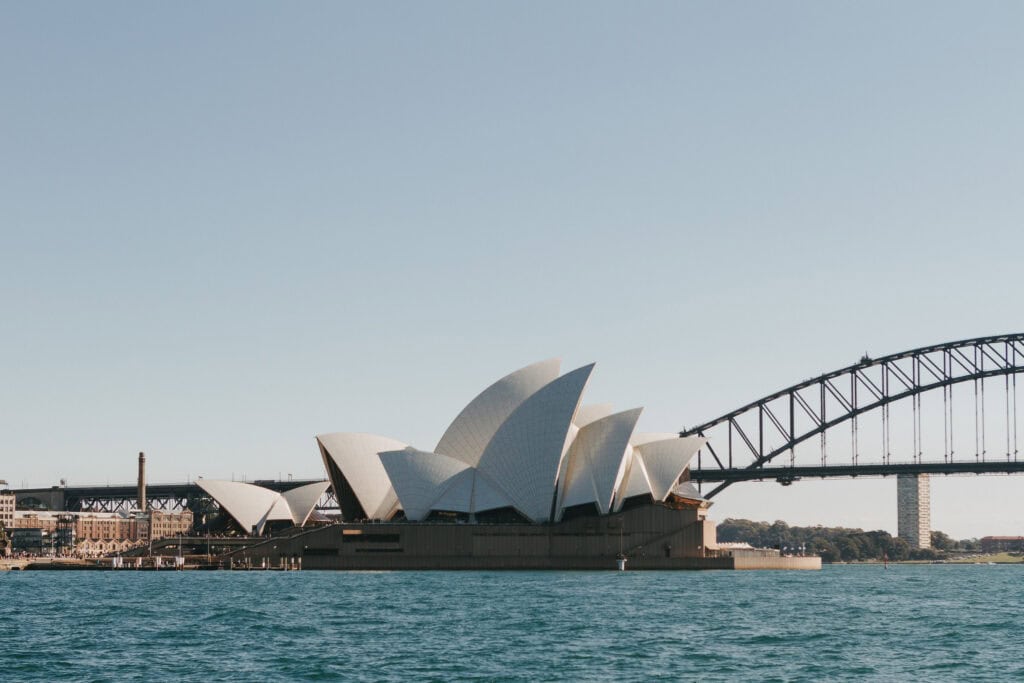 Sydney opera house, with the Sydney Harbour Bridge in the background on a blue sky day. 