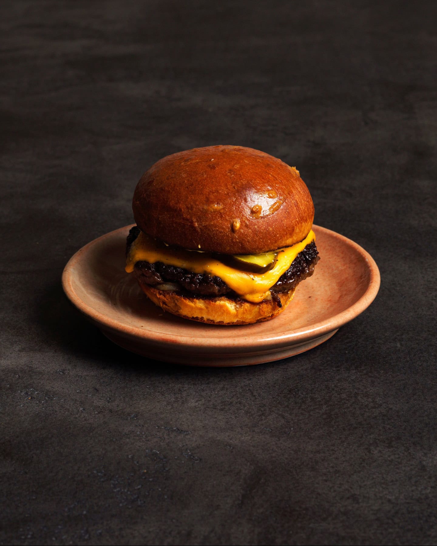 A smash cheeseburger with melted American cheese and pickles on a brioche bun, served on a ceramic plate at Arkhe, Adelaide.