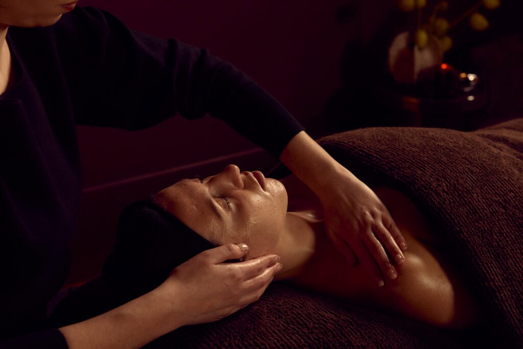 Close-up of a facial treatment at Fluffy Skin in Cremorne, with a therapist massaging a client's neck and décolletage in a softly lit burgundy treatment room.
