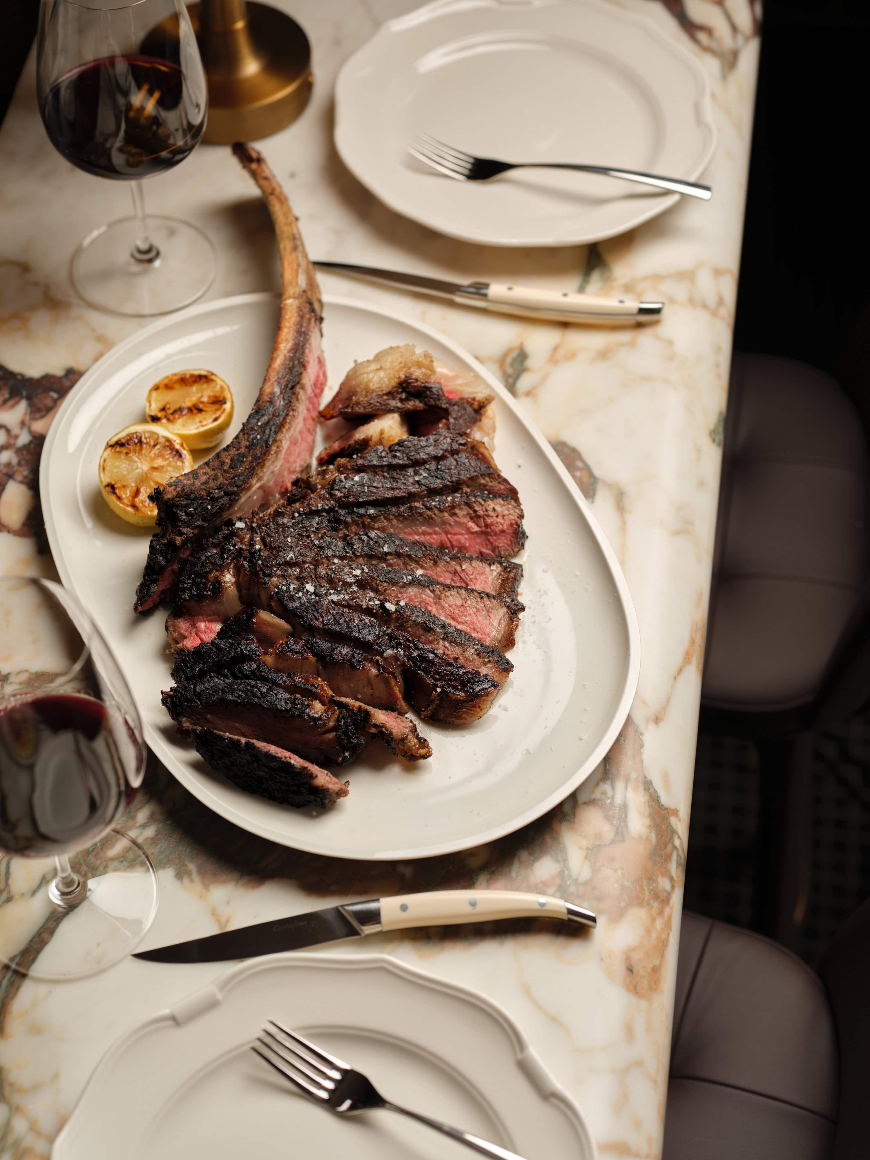 Shiro Kin Full Blood Wagyu Tomahawk and glass of red wine on marble countertop with white plates in grappa sydney the rocks
