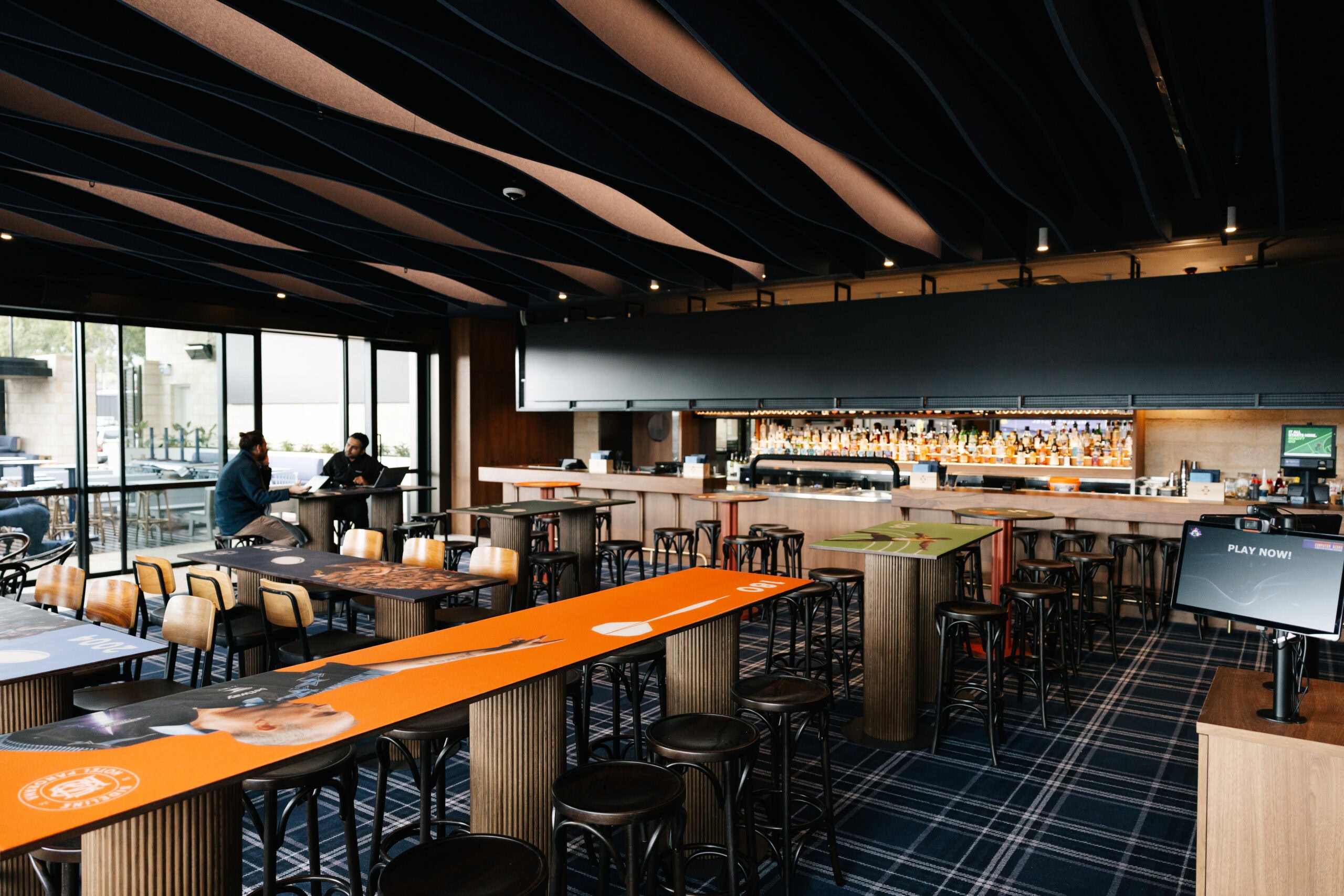 Sideline Bar's interior at Hotel Panorama, featuring long communal tables, bar stools and a well-stocked back bar.