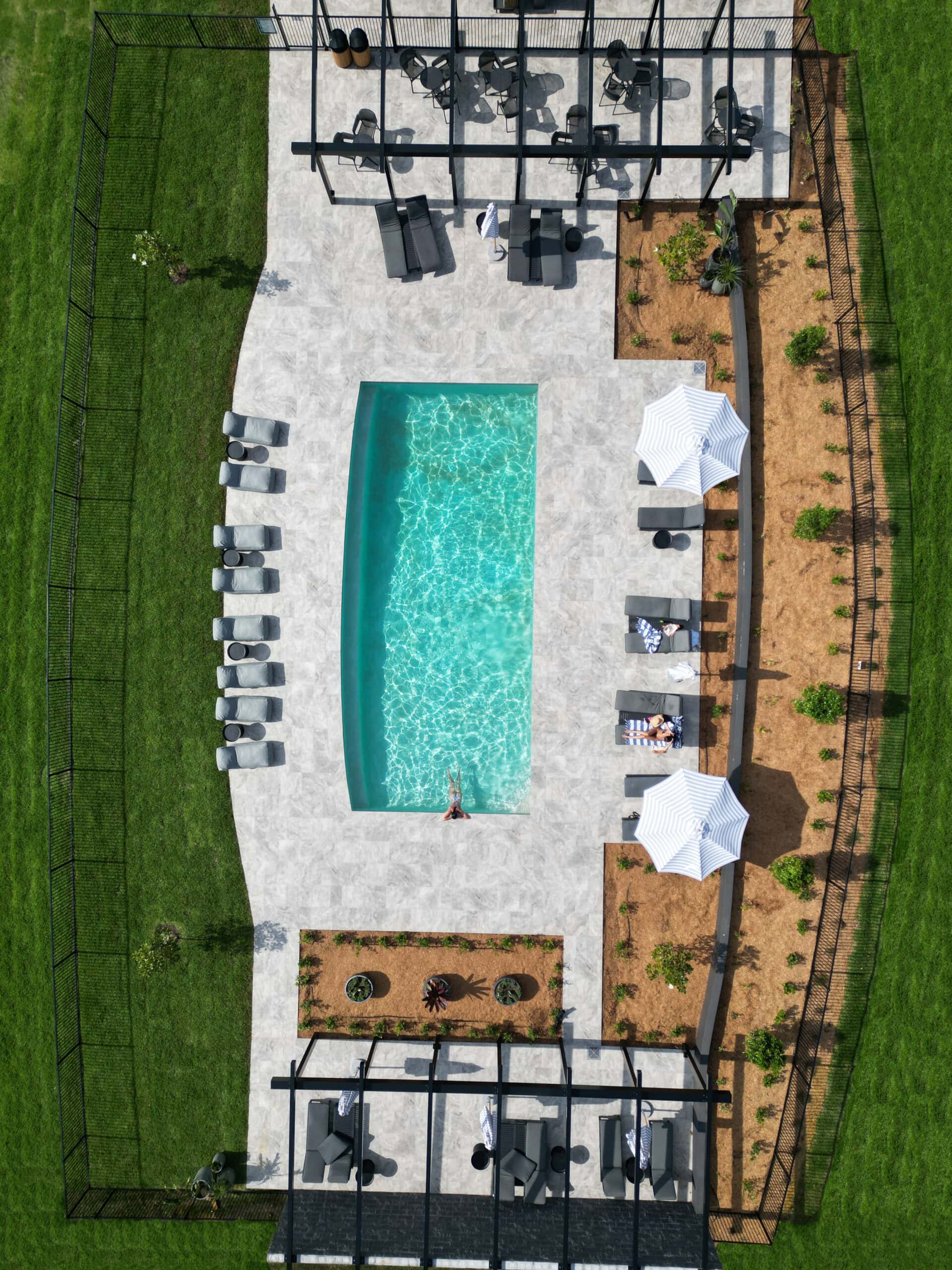 Aerial view of resort pool with sun loungers striped umbrellas and pergola cabanas at The Lane Retreat Pokolbin Hunter Valley