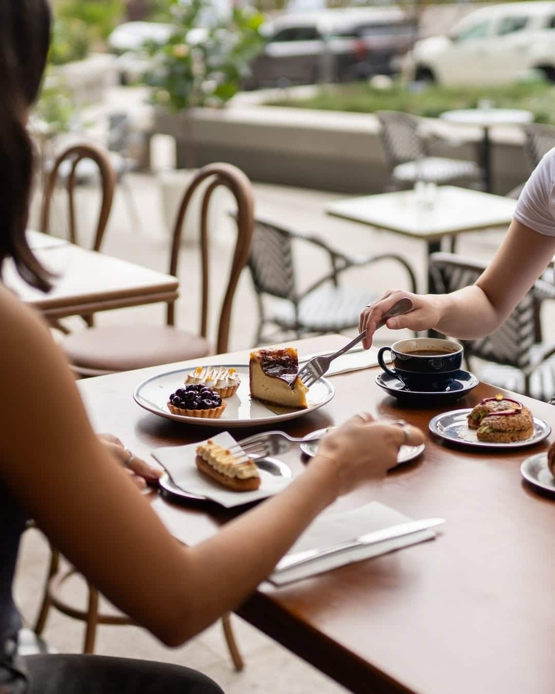 Two people with coffees and cakes at a wooden table at loulou in North Sydney.