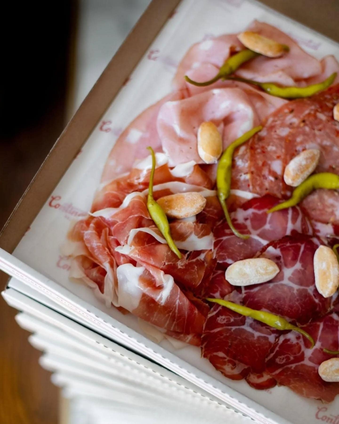 a takeaway box stacked with charcuterie and peppers from continental deli.