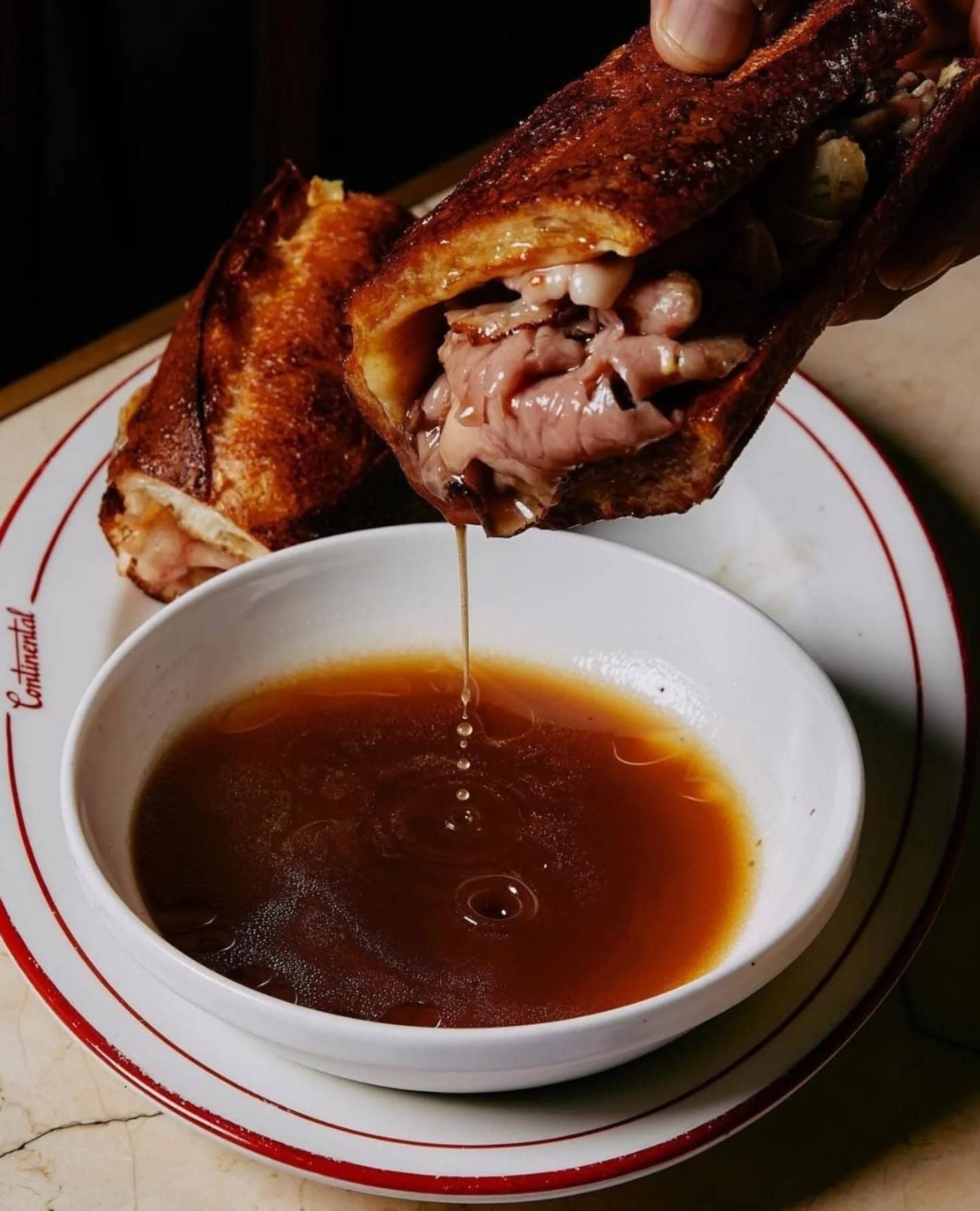 A french dip sandwich being dipped into sauce at continental deli in newtown.